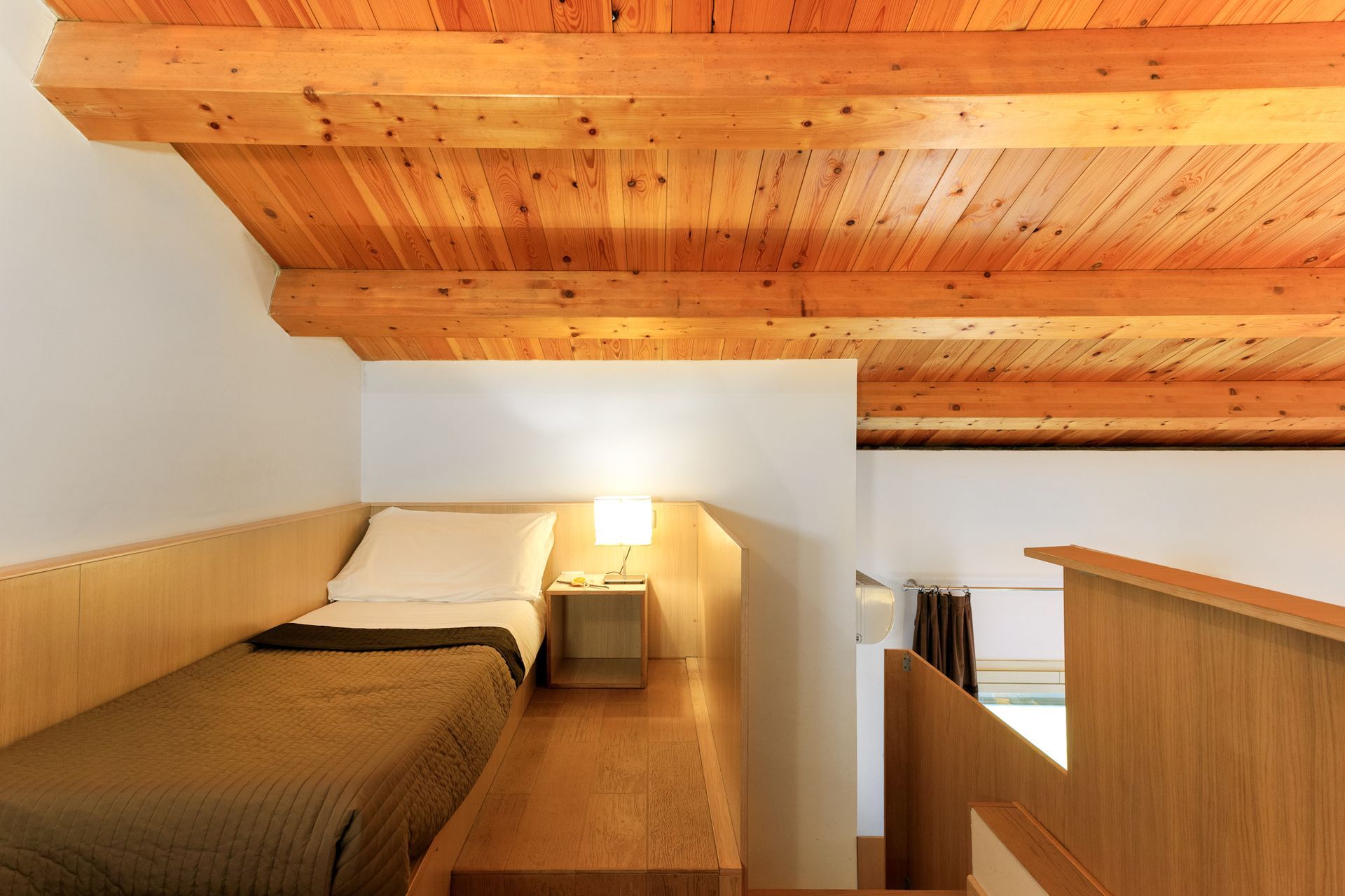 Camera da letto soppalcata con soffitto in legno, due letti e parete divisoria bianca.
