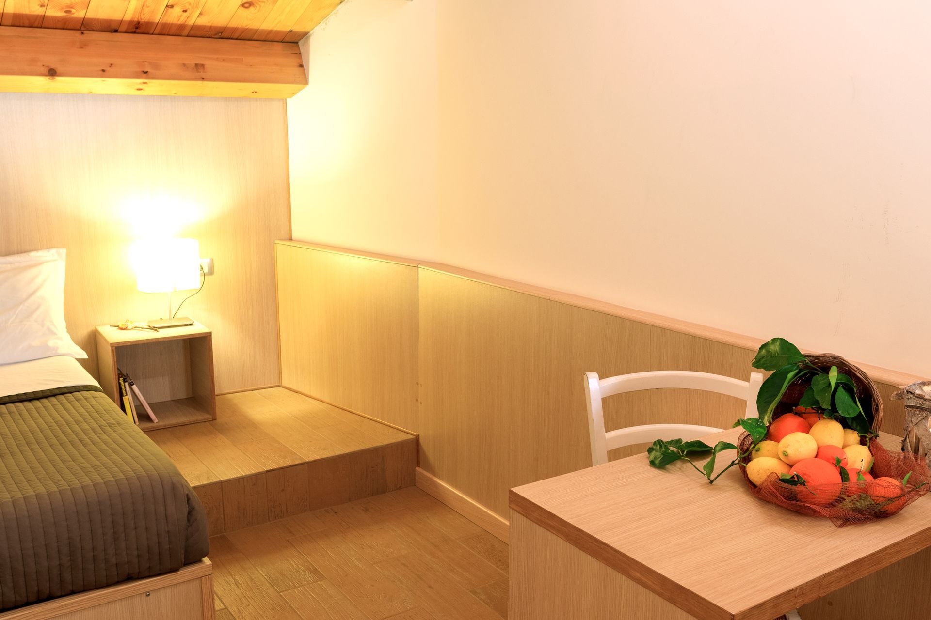 Accogliente camera da letto con letto, lampada da comodino, dettagli in legno e un tavolino con frutta in primo piano.