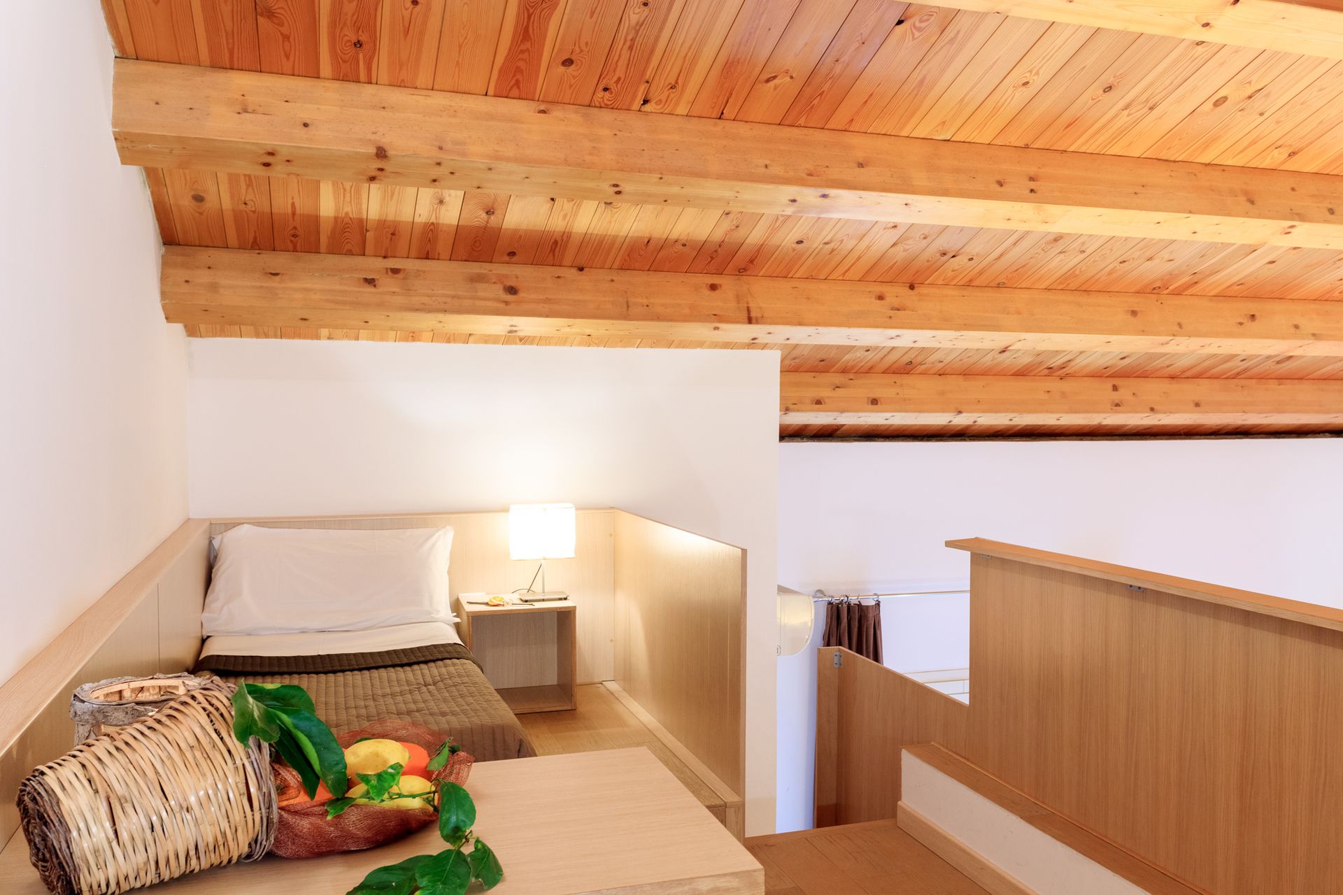 Camera da letto soppalcata con soffitto inclinato rivestito in legno e angolo letto.