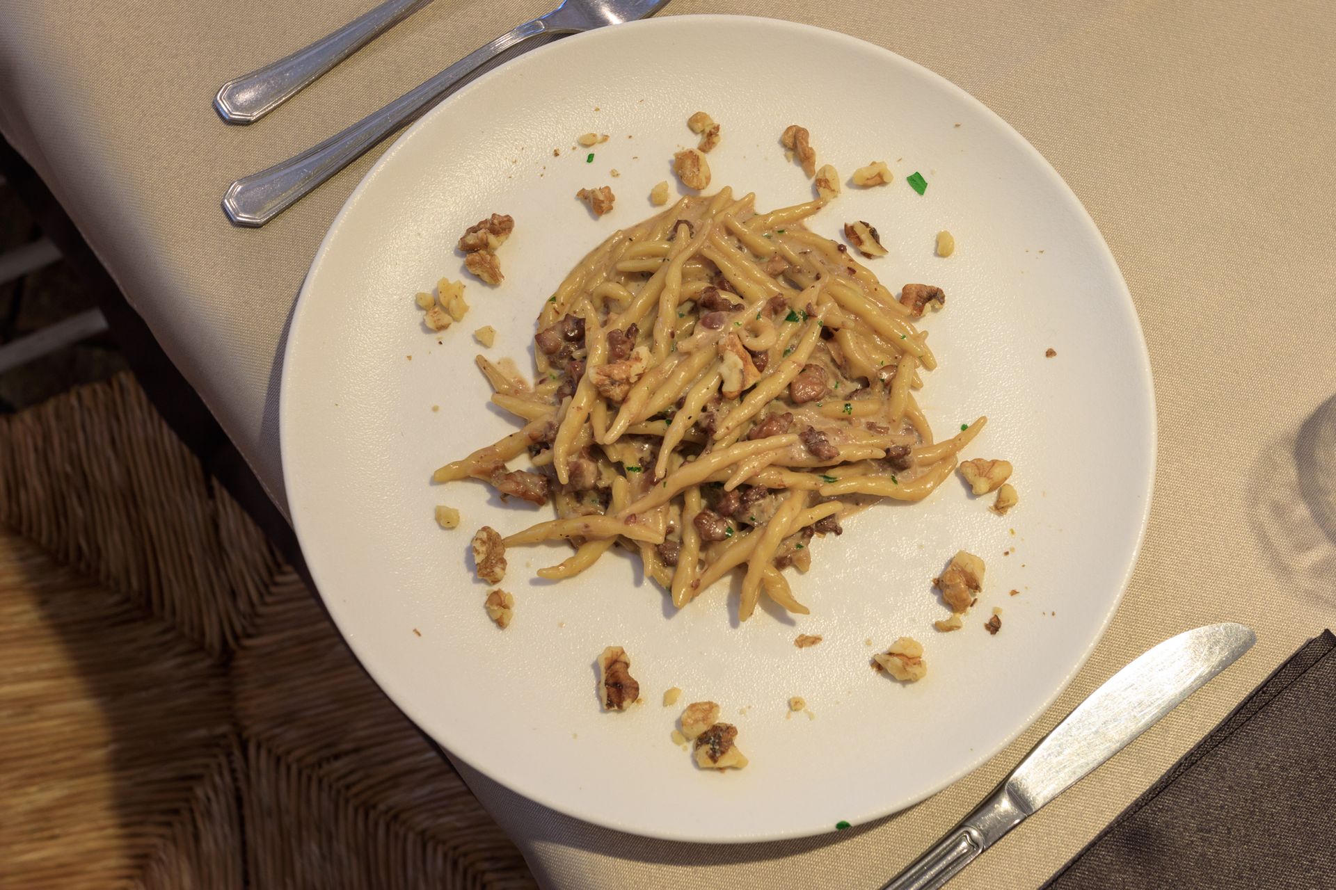 Pasta parzialmente mangiata su un piatto bianco con posate su una tovaglia.