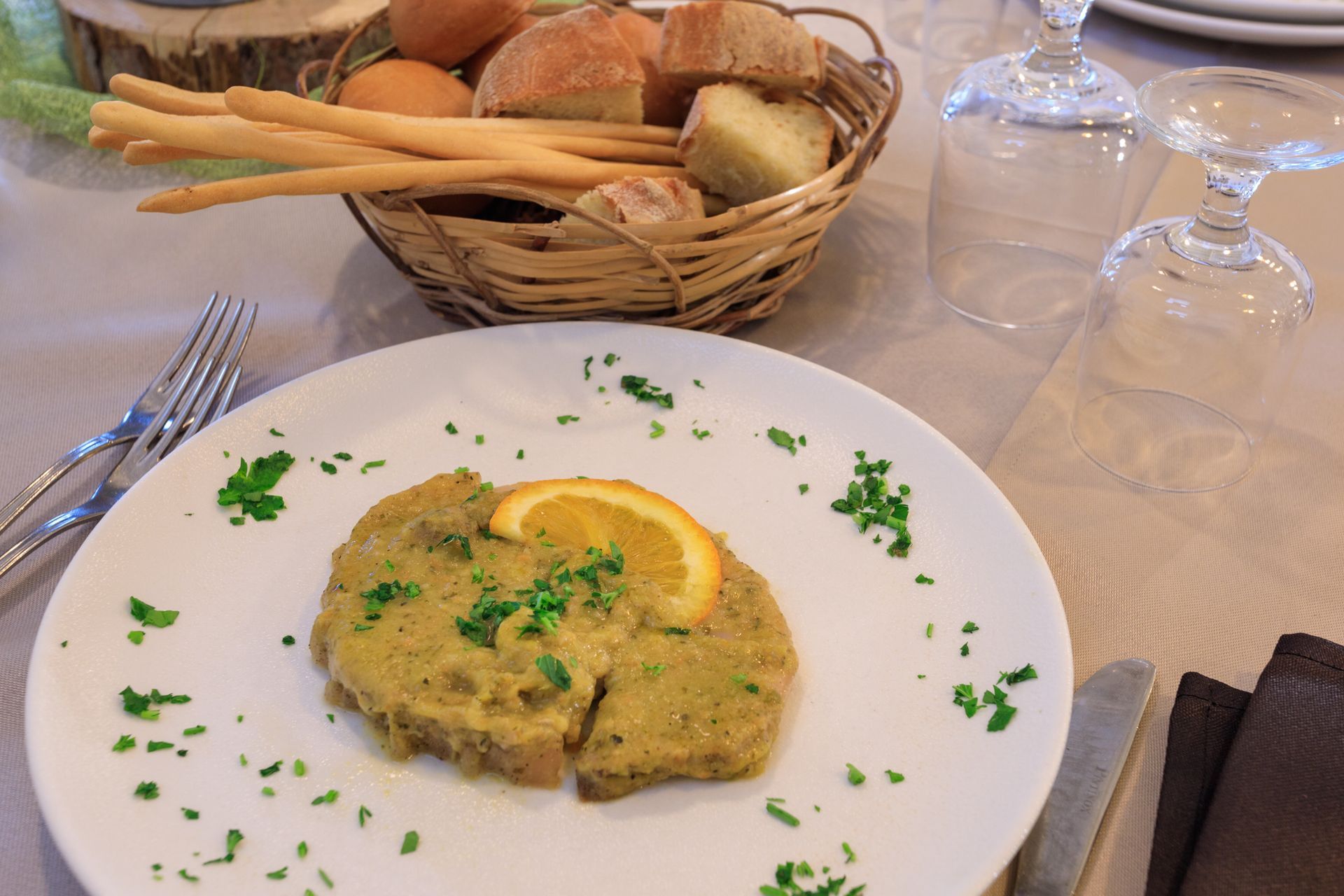Piatto di cibo salato con guarnizione di limone e prezzemolo, su un tavolo da pranzo con cestino del pane e bicchieri.