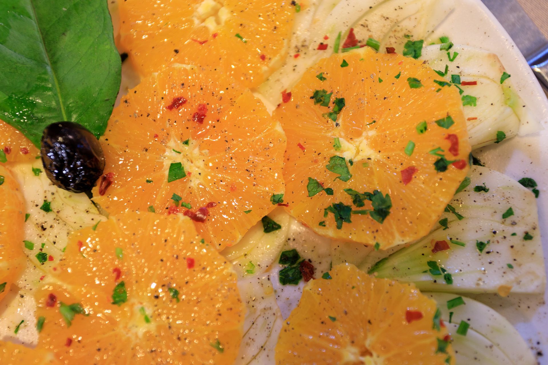 Insalata di agrumi bianchi e arancioni con erbe aromatiche e un'oliva nera su un piatto bianco.