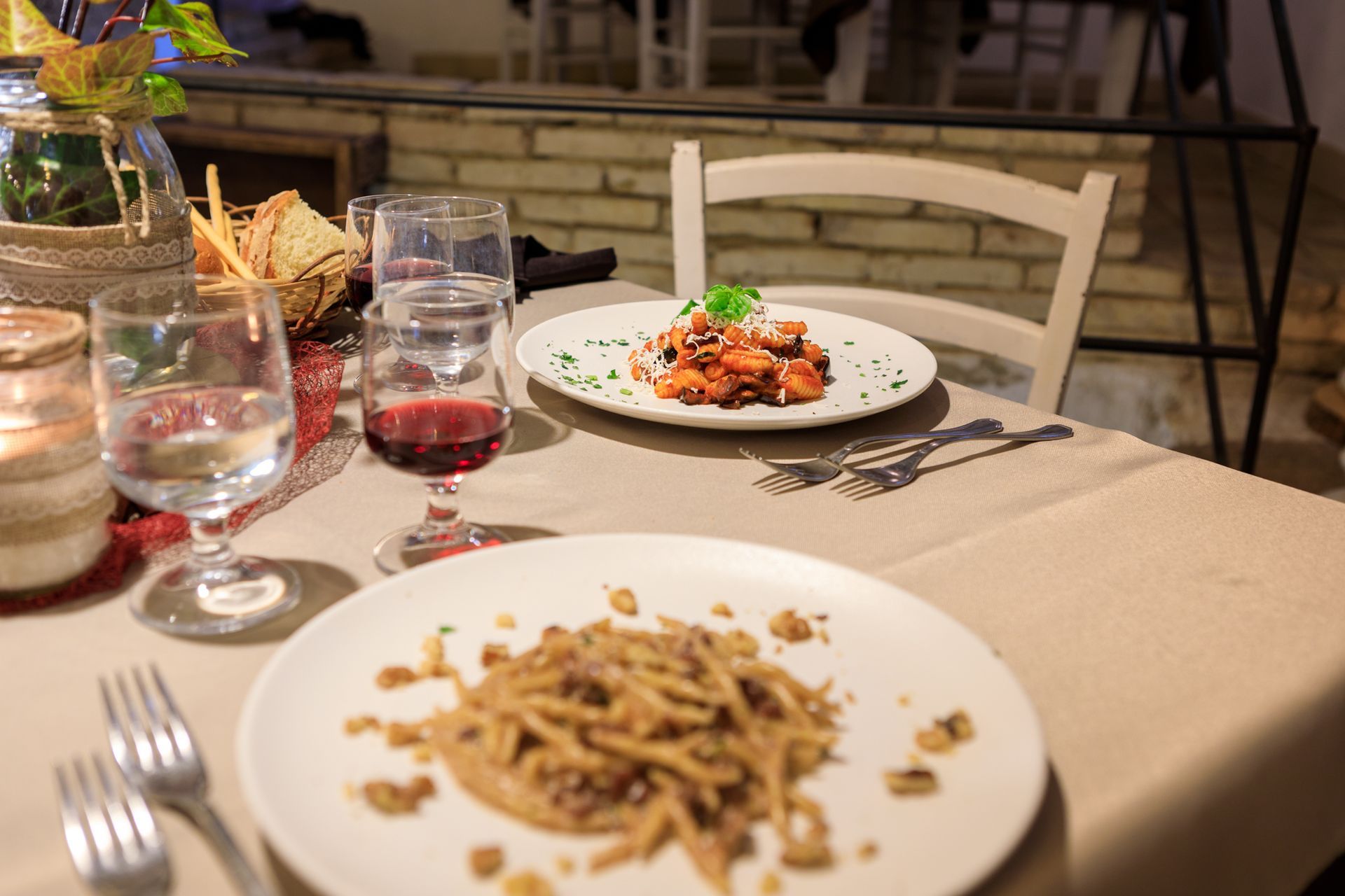 Tavolo da pranzo apparecchiato con pasta, bicchieri d'acqua e un calice di vino in un ambiente da ristorante.
