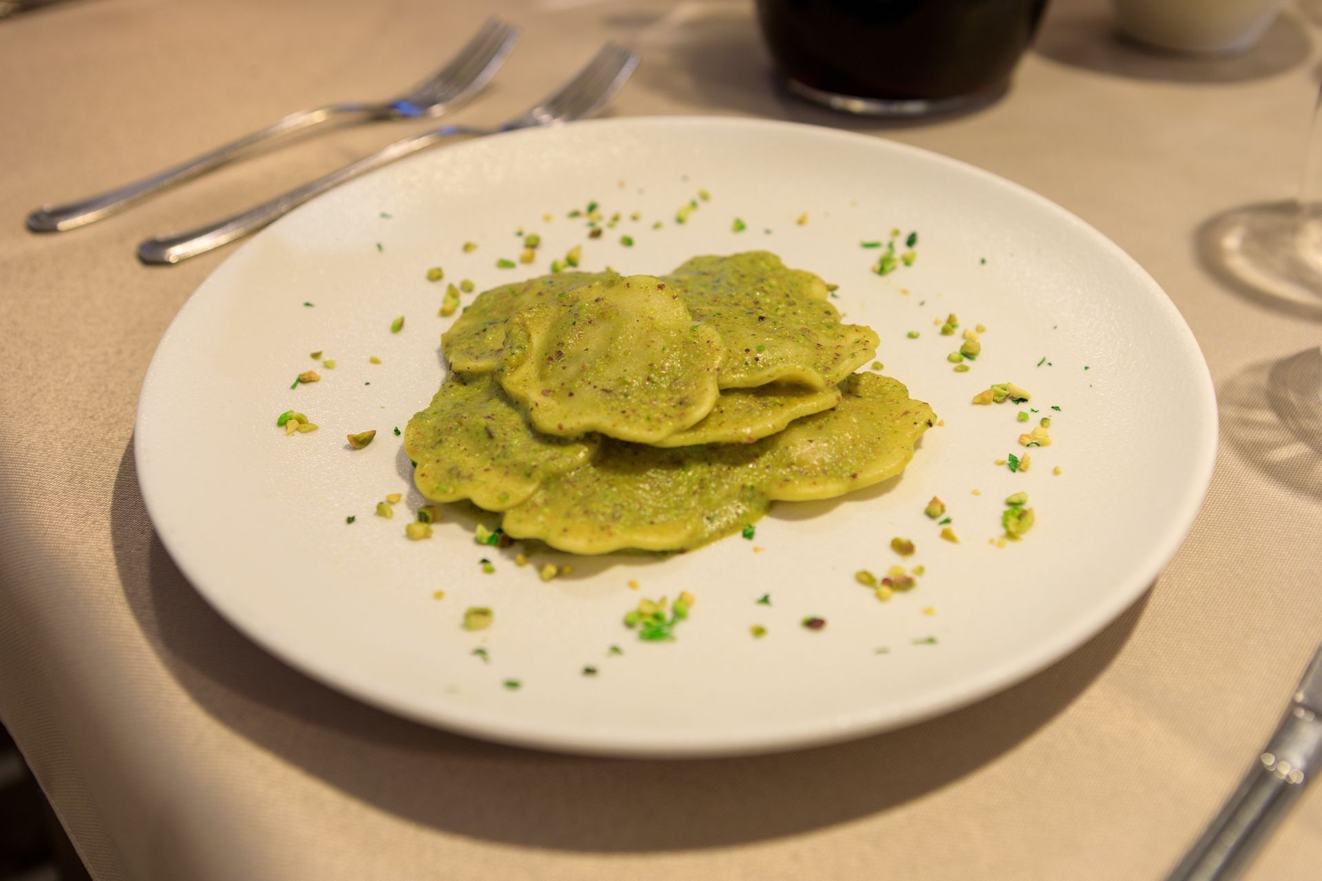 Piatto di ravioli verdi guarniti con erbe aromatiche su un tavolo di ristorante.