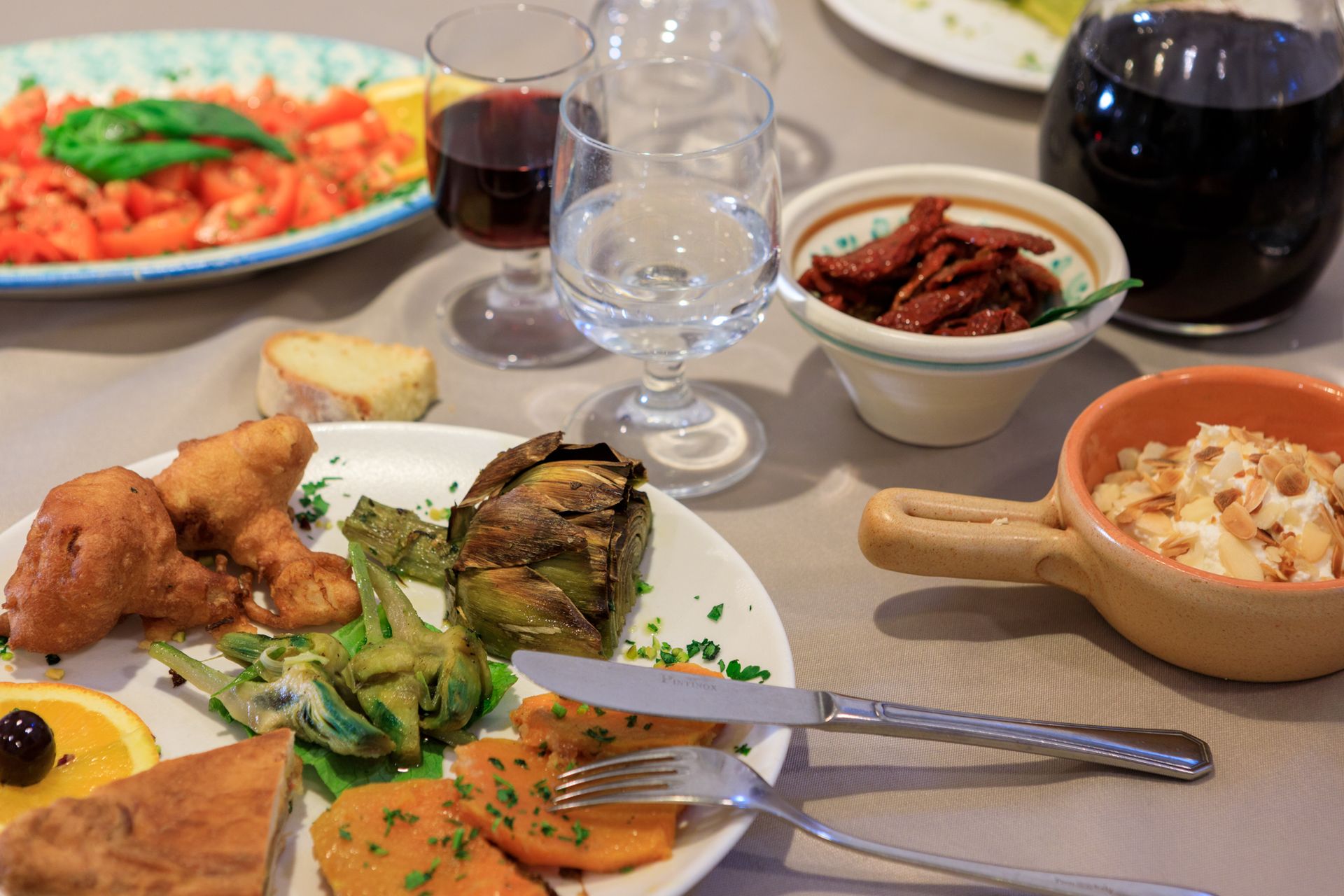 Tavolo con piatti, bicchieri e posate assortiti, apparecchiati per un pasto condiviso.