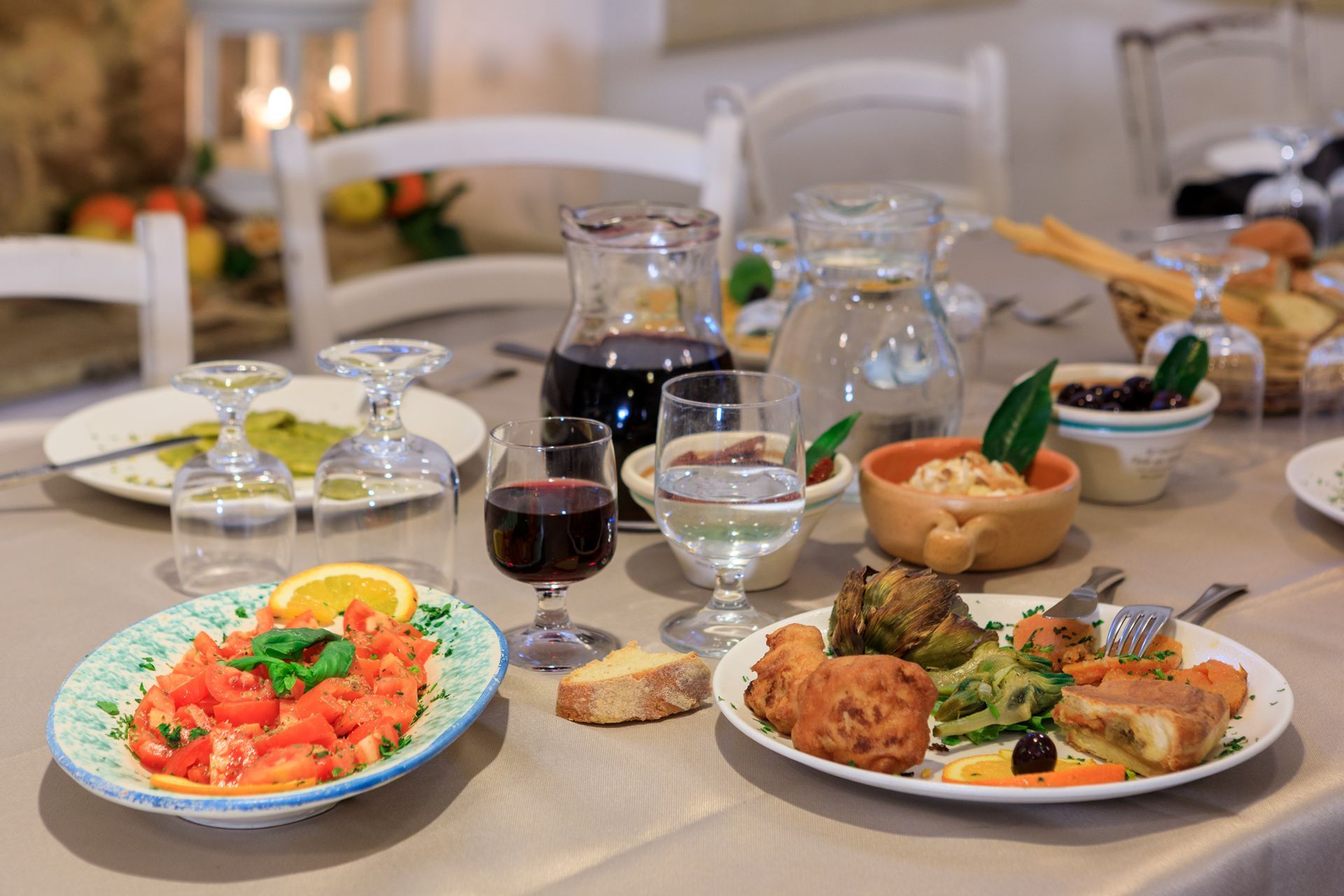 In un luminoso ristorante, la tavola è apparecchiata con piatti di pesce, bicchieri da vino, pane e caraffe.