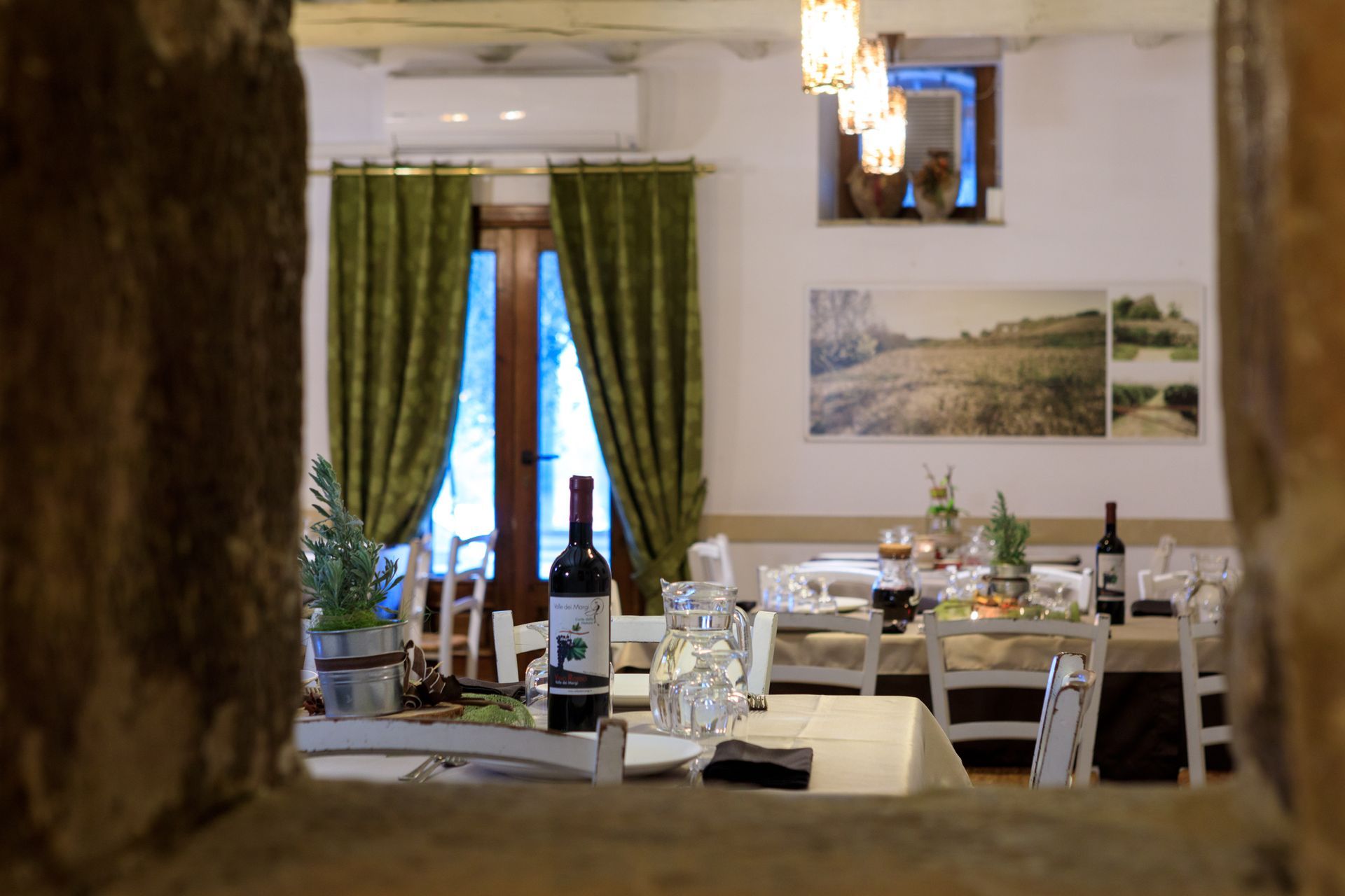 Elegante sala da pranzo con tavoli apparecchiati, bottiglie di vino, tende verdi e uno specchio a parete.