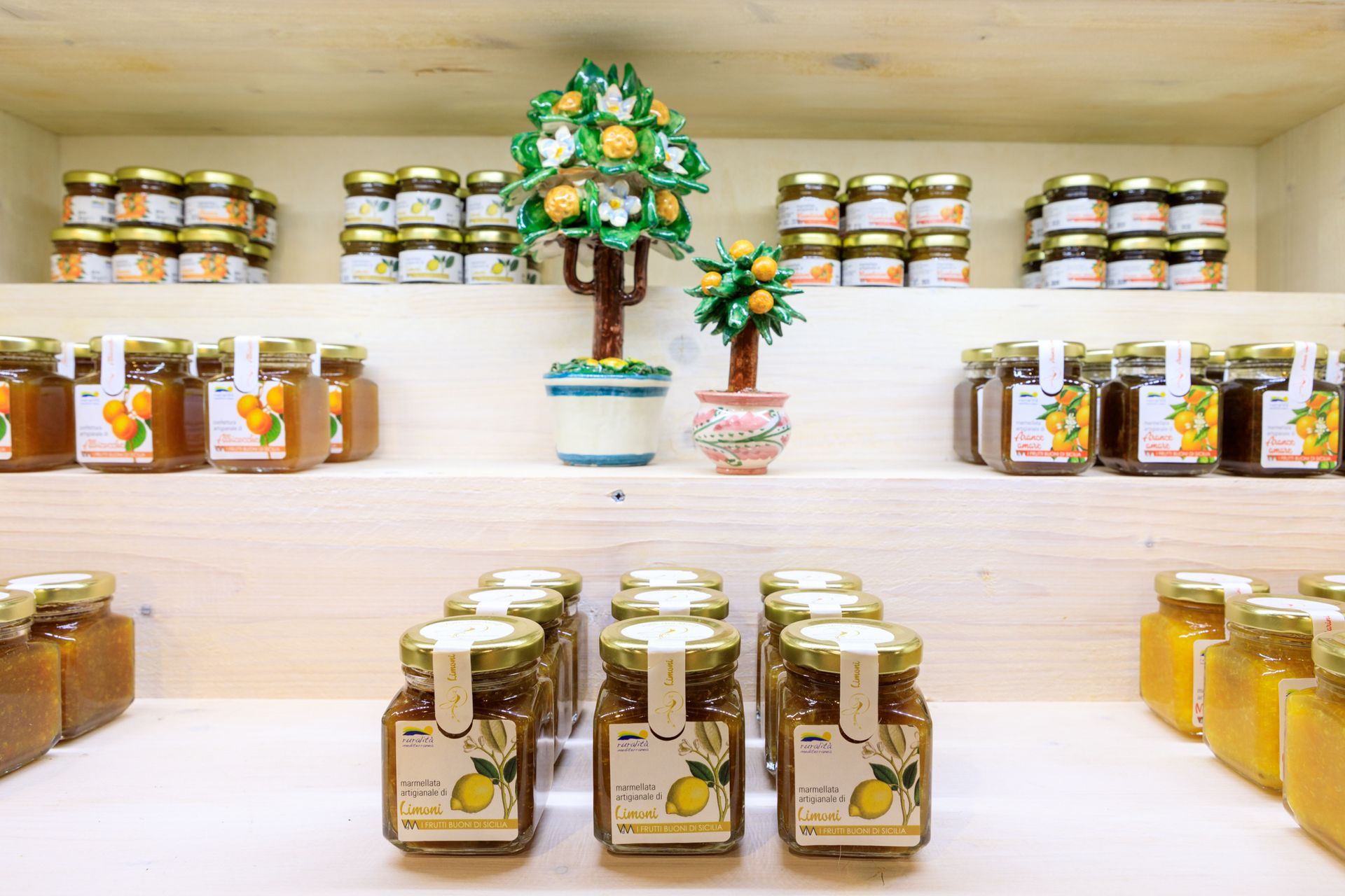 Barattoli di conserve e miele esposti su scaffali bianchi in un luminoso interno di negozio.