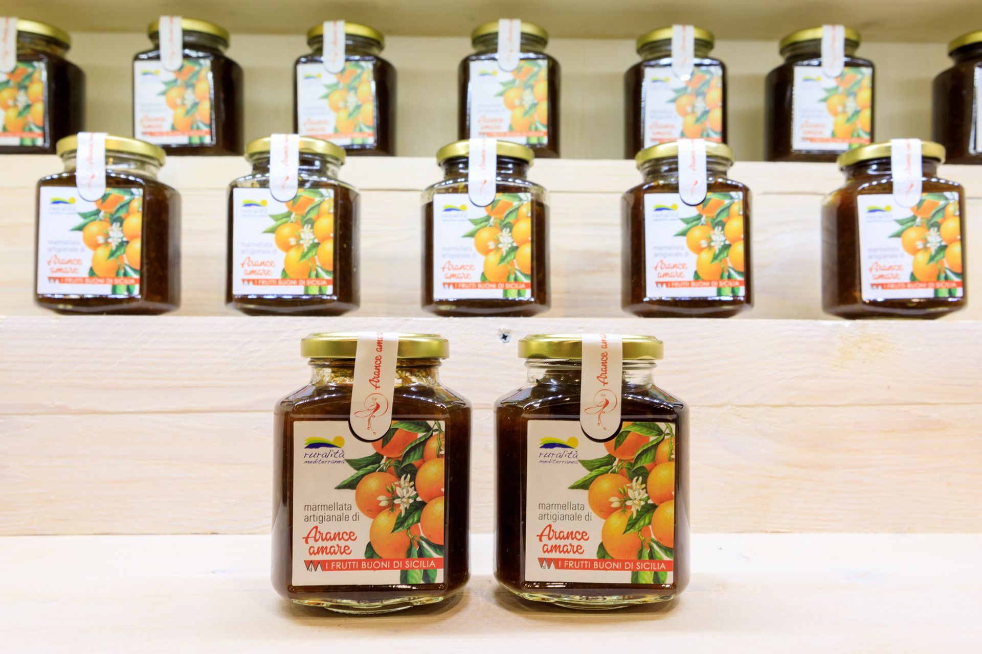 File di piccoli vasetti di vetro con etichette color beige e cucchiaini di legno, disposti su scaffali bianchi.