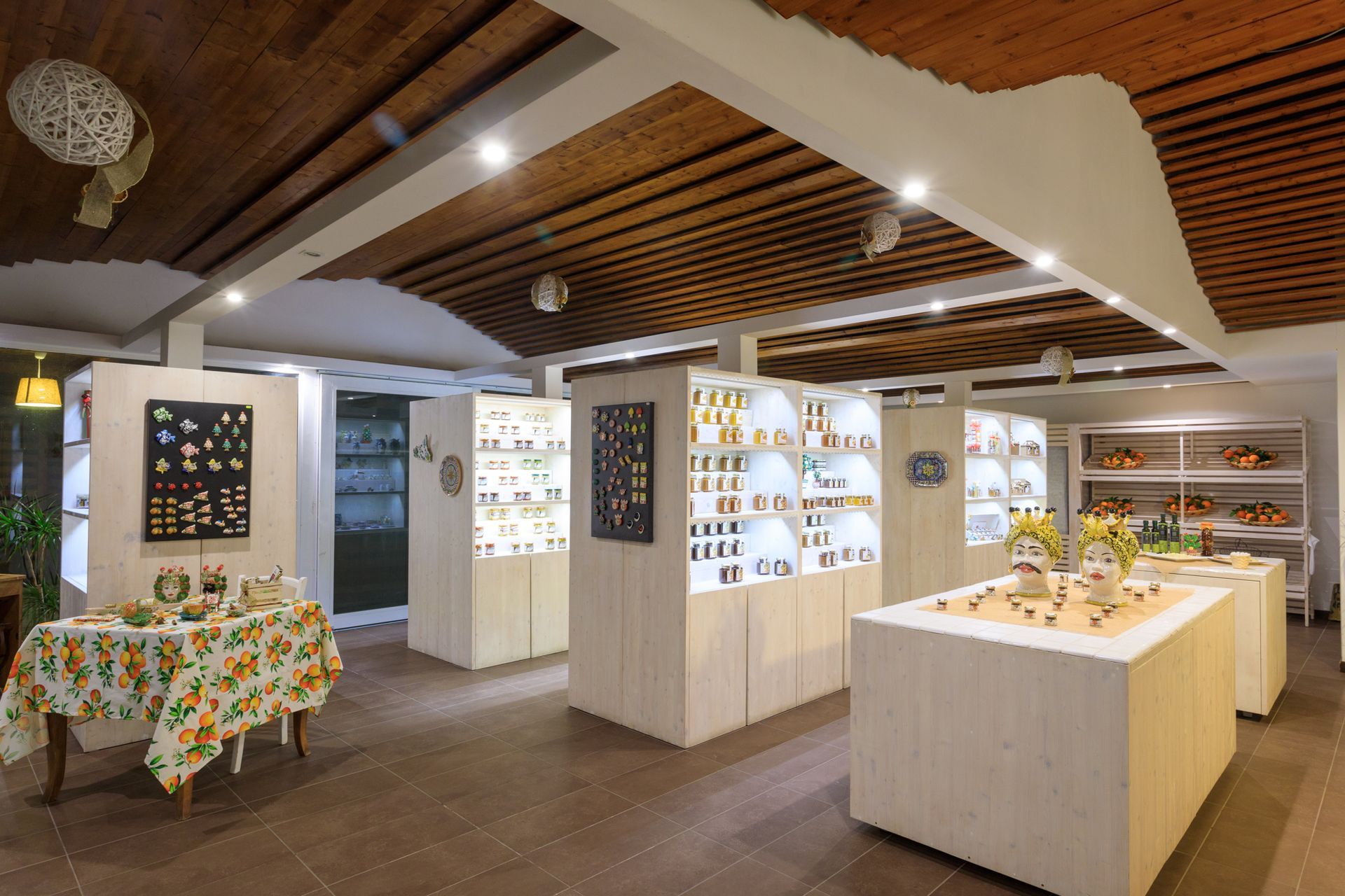 Interno luminoso di una gioielleria con vetrine bianche, lampade a sospensione e soffitto a doghe di legno.