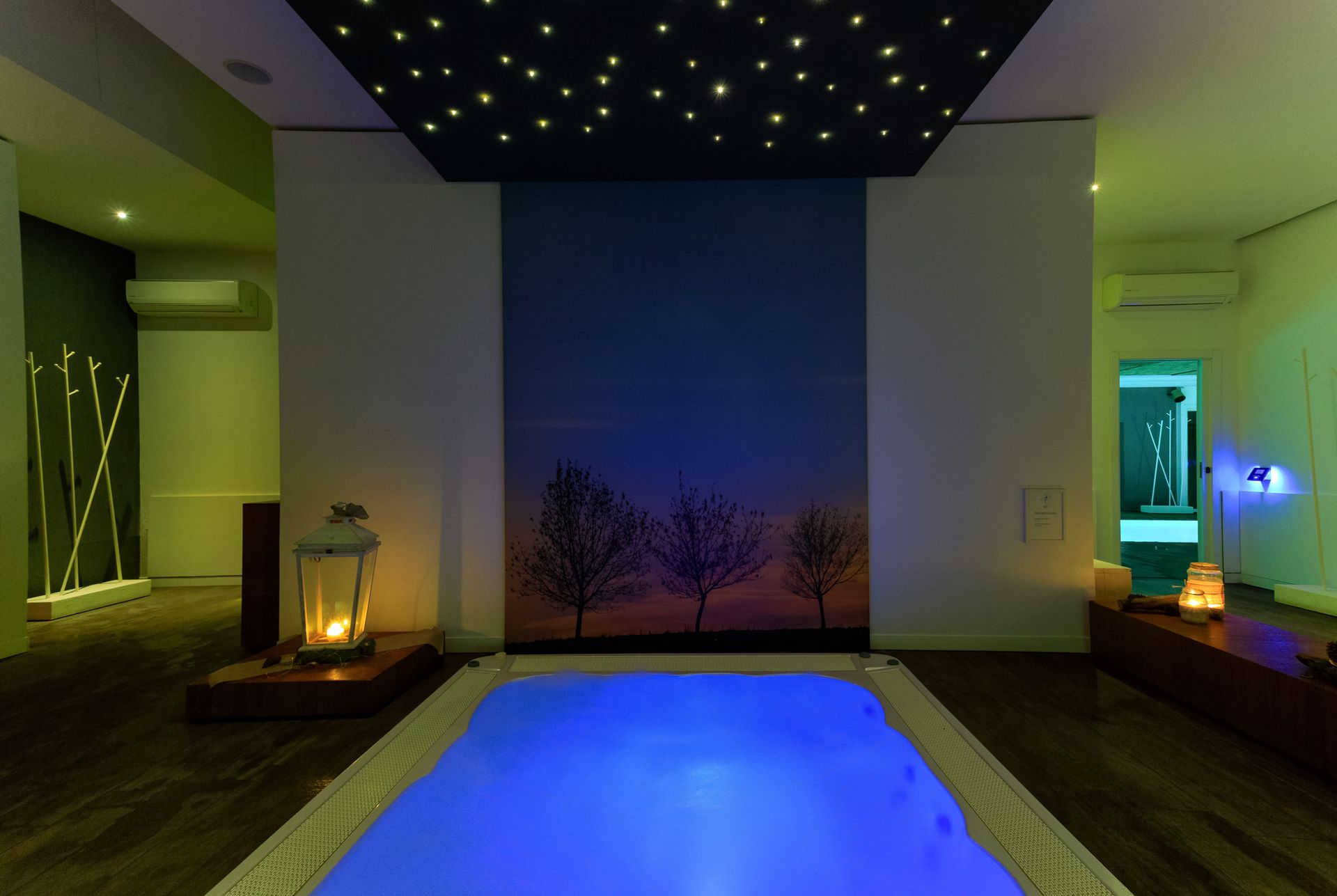 Sala spa interna con piscina blu luminosa, lanterne e luci a soffitto che ricordano le stelle.