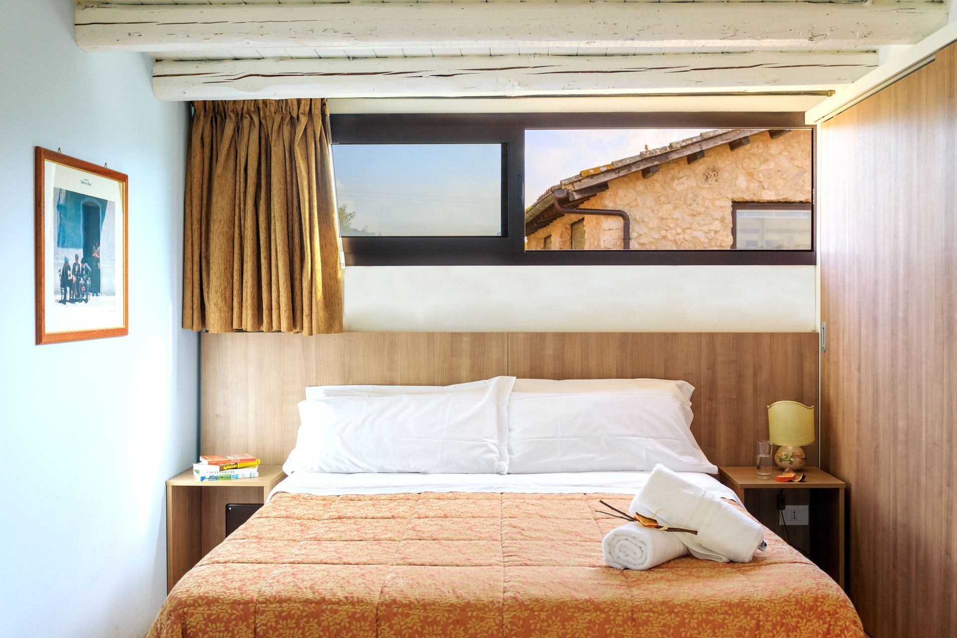 Camera da letto compatta con letto, lenzuola bianche, copriletto beige e finestra sopra la testiera.