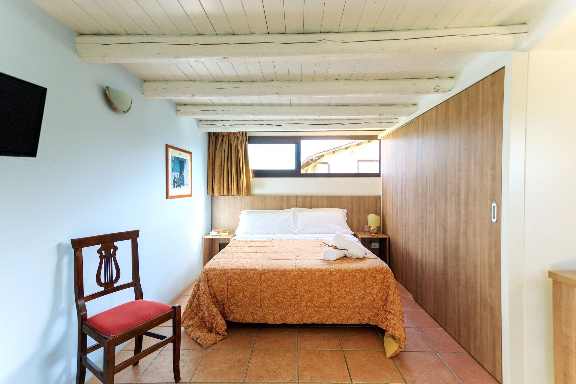 Semplice camera da letto con letto, armadio in legno, sedia e finestra luminosa