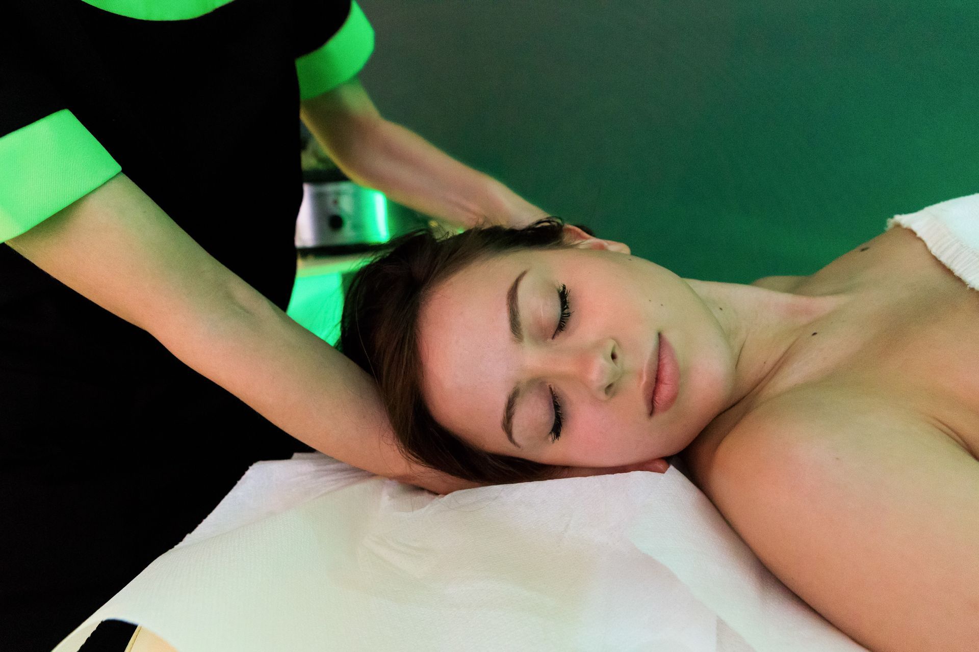 Persona che riceve un massaggio al collo su un lettino da trattamento, in un'atmosfera da spa illuminata di verde.