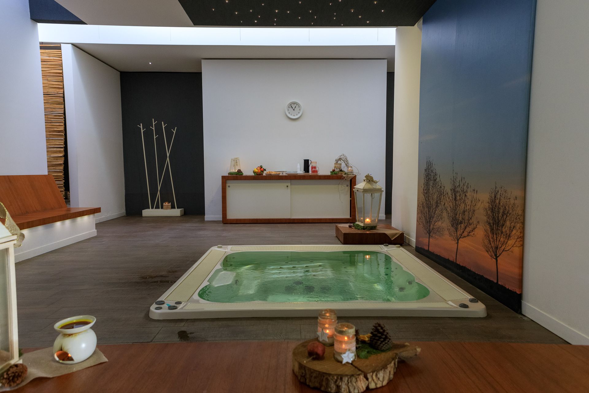 Moderna sala spa con piscina quadrata rialzata, candele, arredamento minimalista e interni dai rilassanti toni grigio-blu.