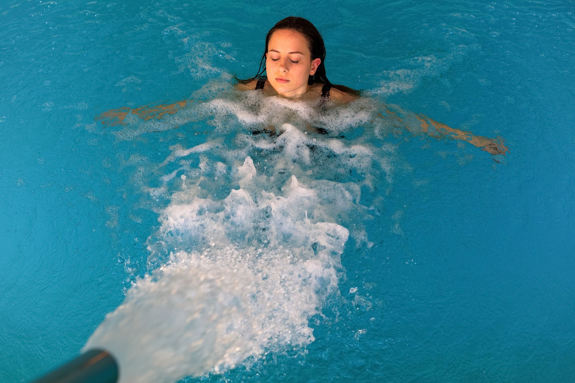 Un nuotatore galleggia in una piscina blu, facendosi strada tra gli spruzzi d'acqua bianca.
