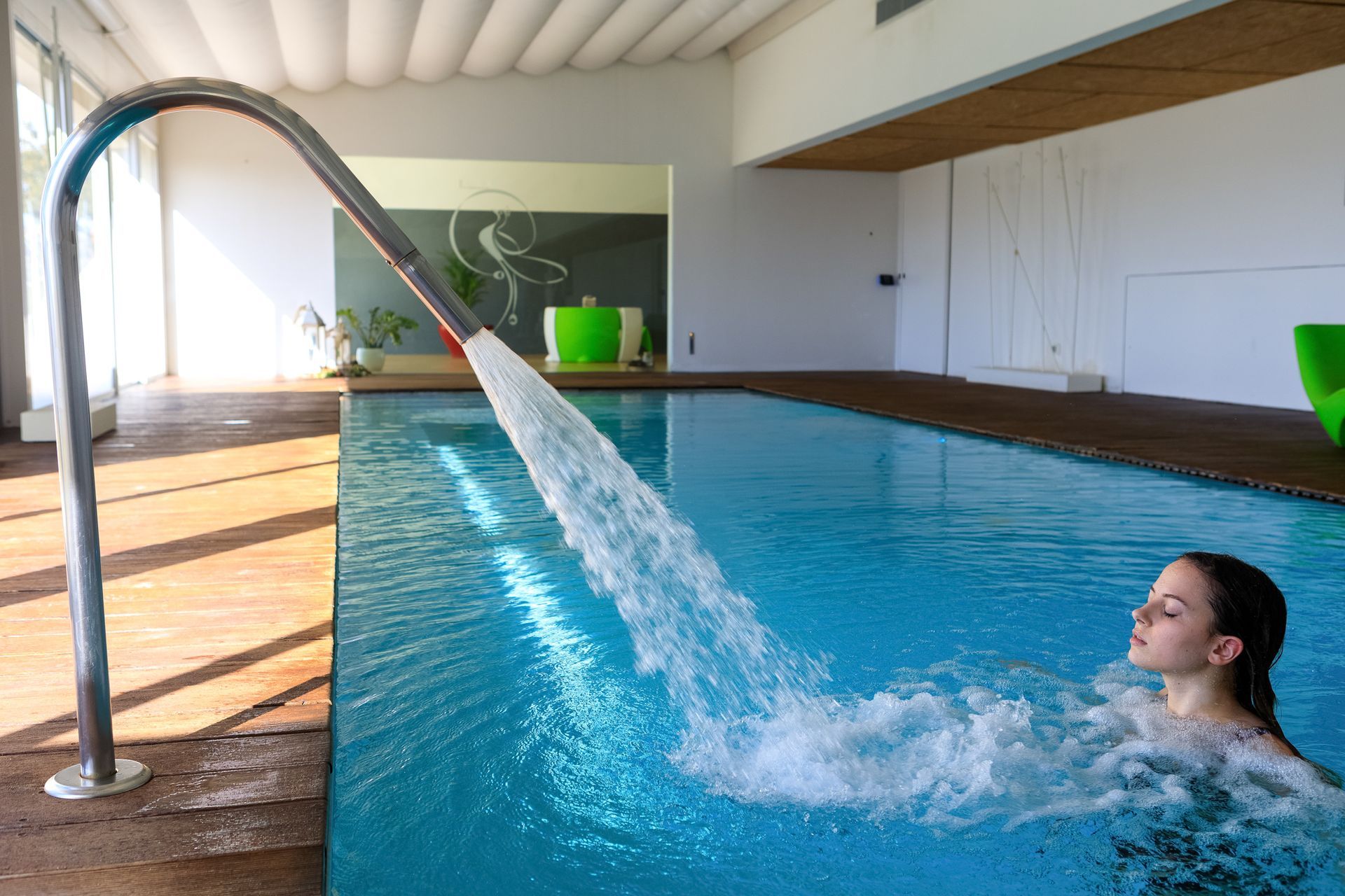 Piscina coperta con una persona che sguazza sotto un getto d'acqua curvo.