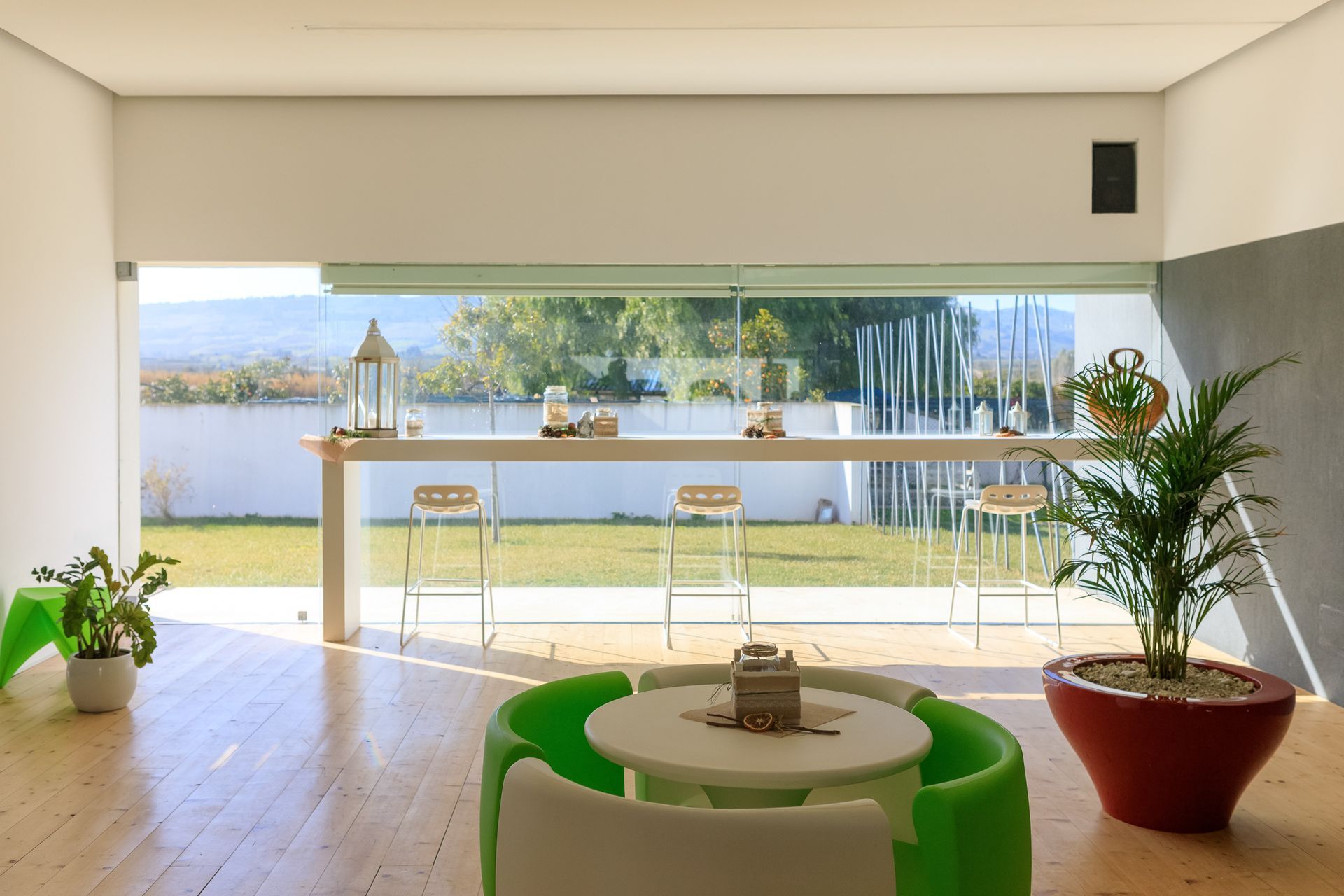 Luminoso soggiorno moderno con sedie verdi, tavolo rotondo e vista sul lago attraverso ampie porte finestre.