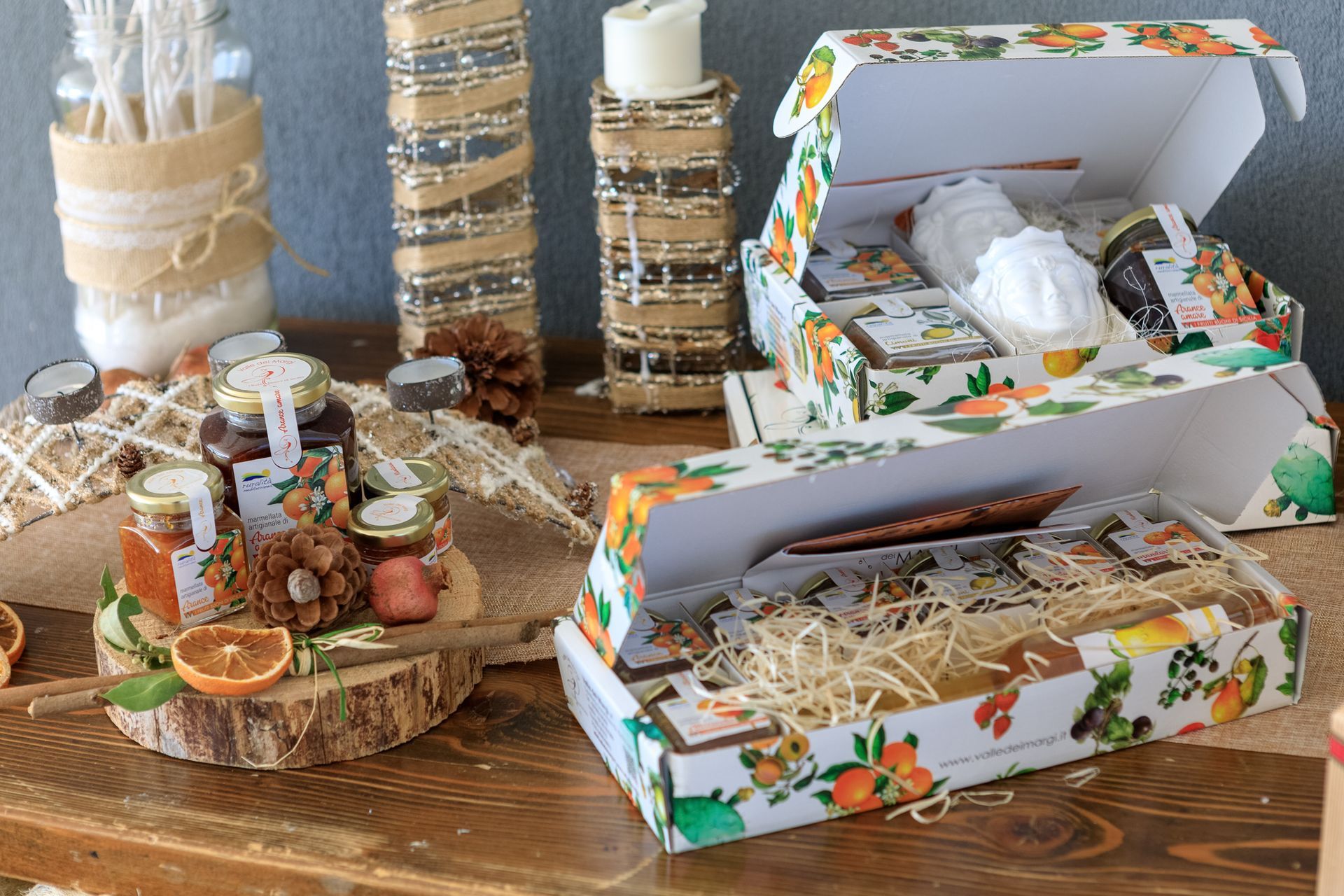 Scatole regalo decorative con stampe floreali e composizioni rustiche di candele su un tavolo di legno.