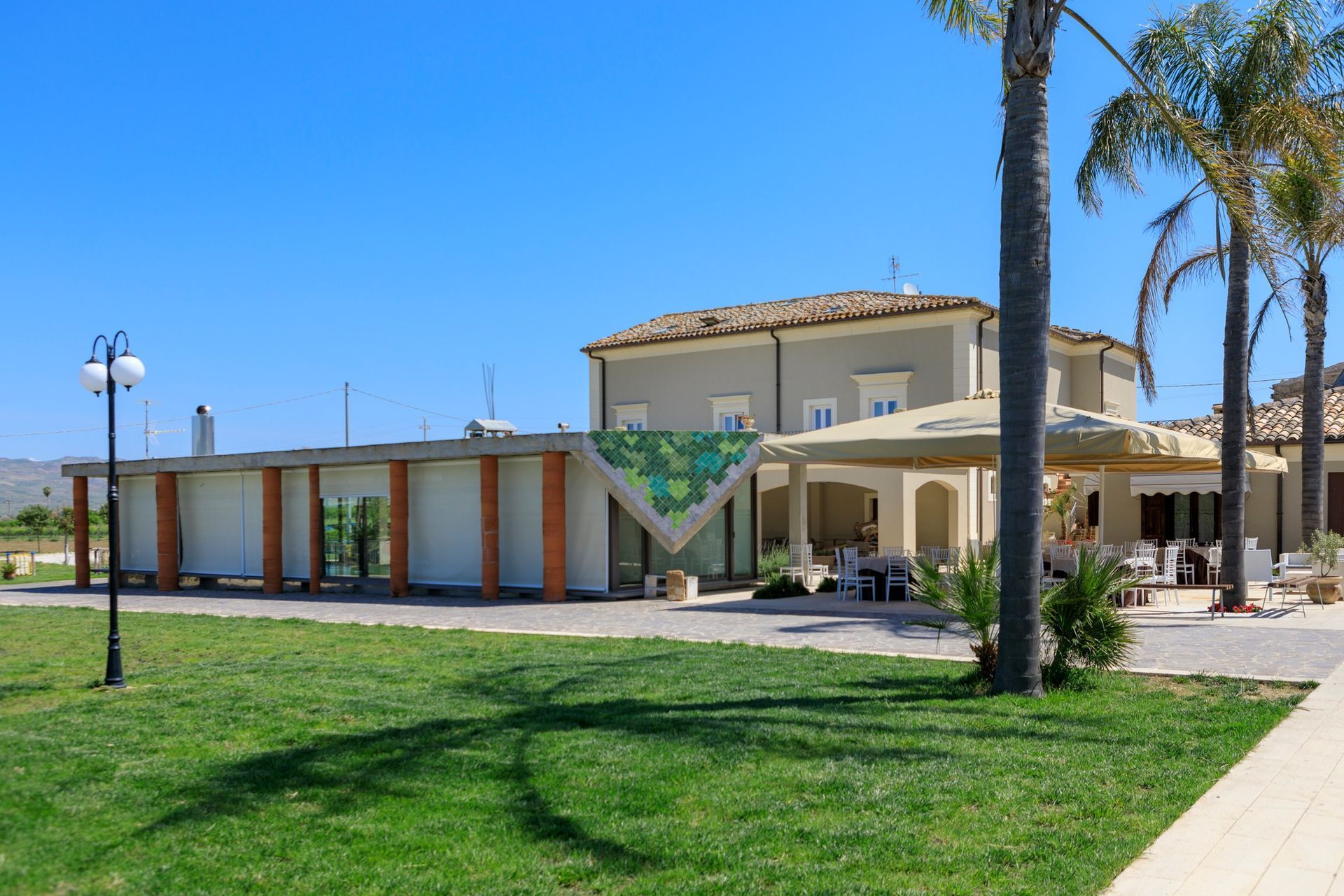 Edificio moderno con palme, un prato verde e un cielo azzurro limpido.