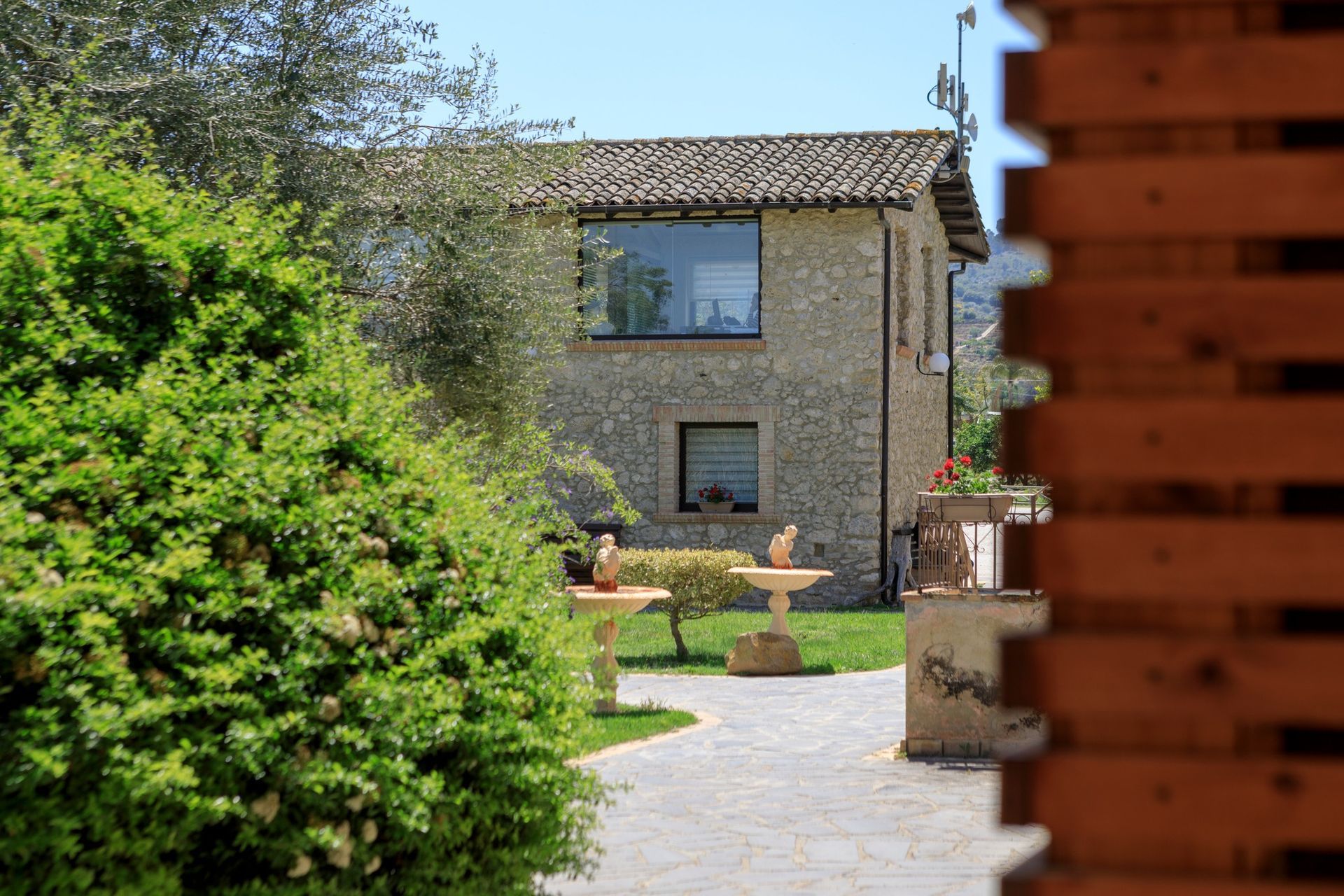 Dehor di un caffè all'aperto con ombrelloni beige e tavolini vuoti accanto a un edificio color crema sotto un cielo azzurro.