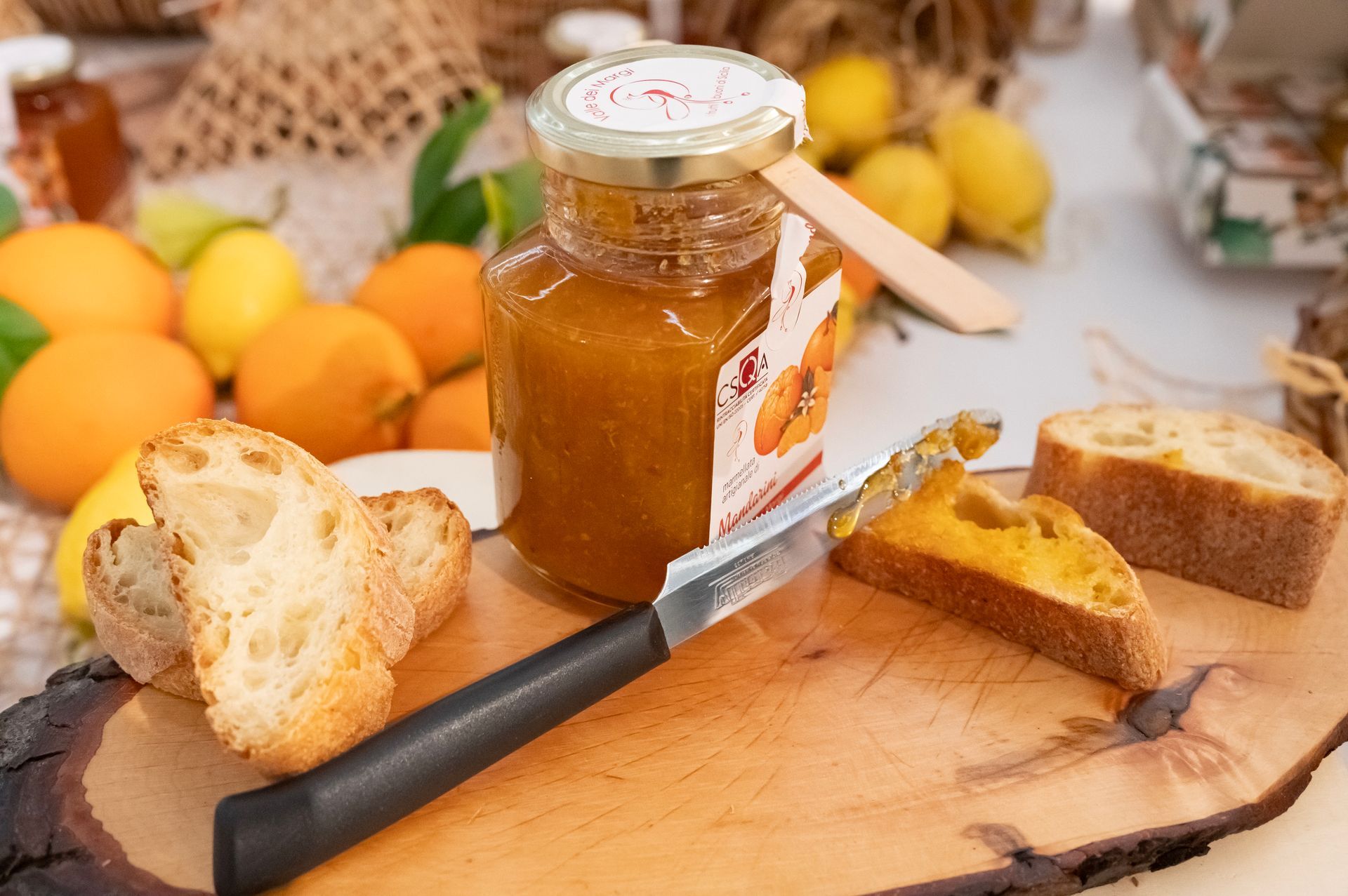 Un barattolo di marmellata e fette di pane su un tagliere, con arance e limoni sullo sfondo.