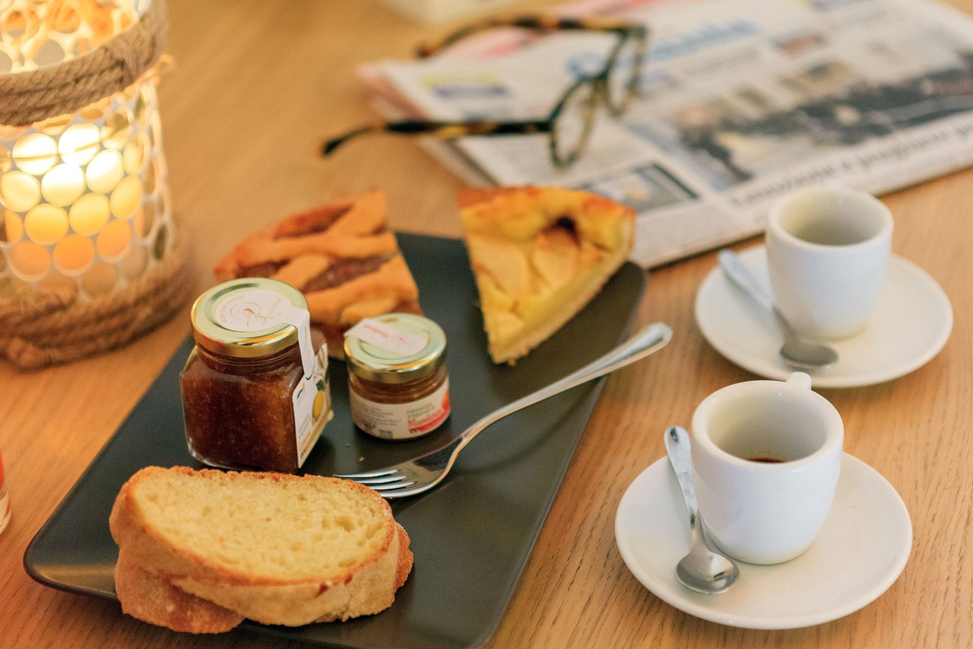 Tavolo della colazione con pane tostato, marmellata, torta e due tazze di caffè su piattini.