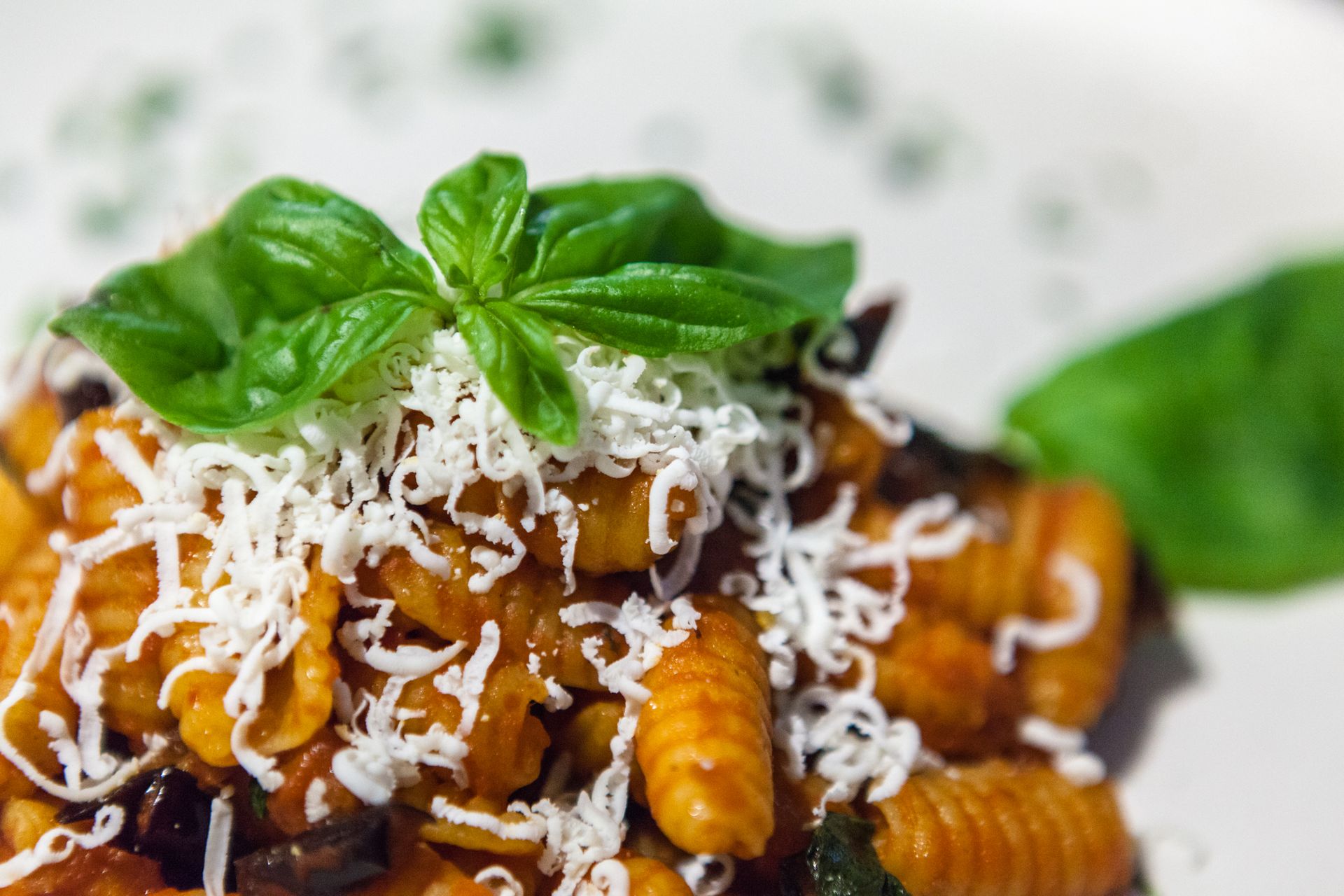 Pasta al sugo di pomodoro, formaggio grattugiato e basilico, servita su un piatto bianco.