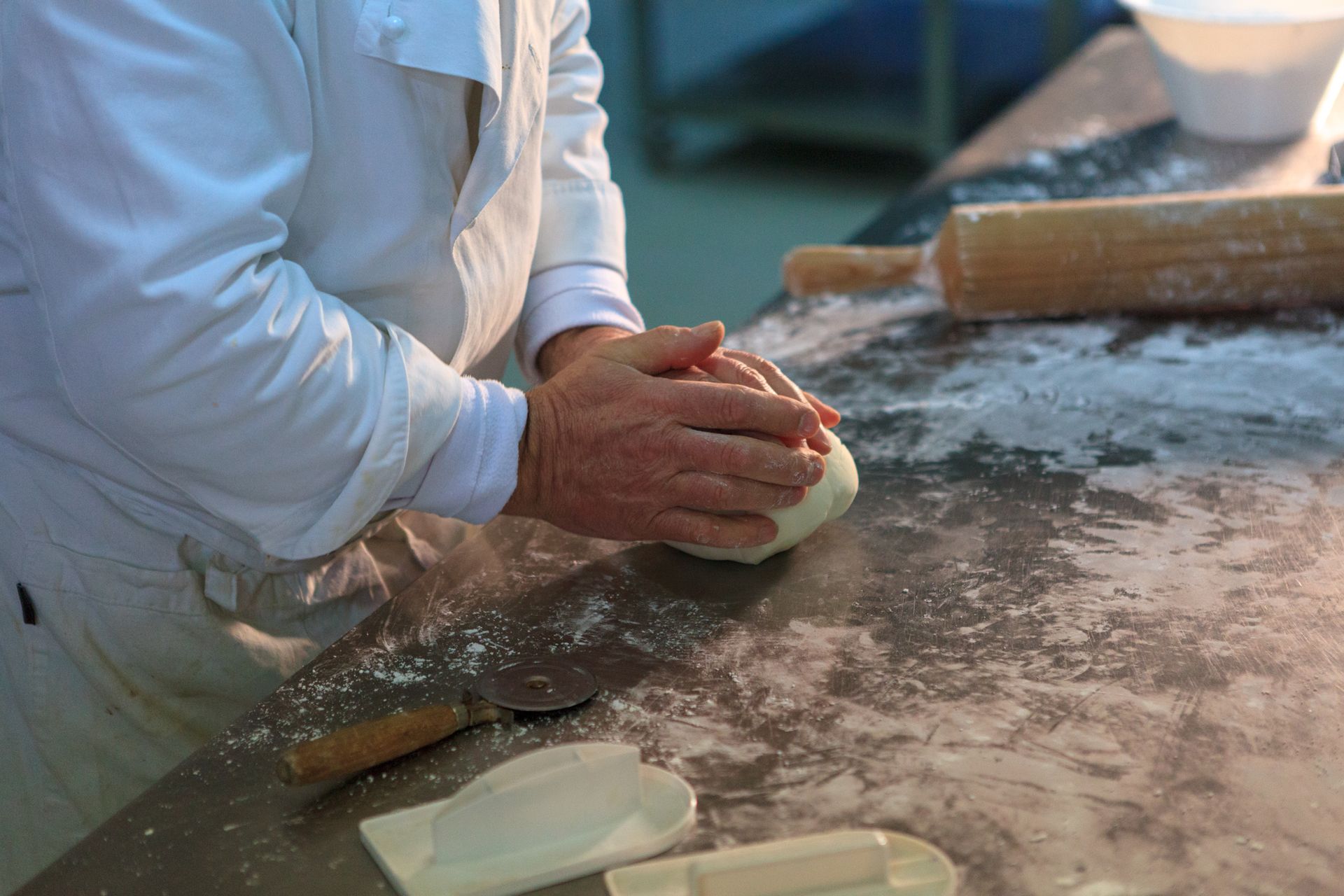 Mani che modellano l'impasto su una superficie di lavoro infarinata con un mattarello nelle vicinanze.