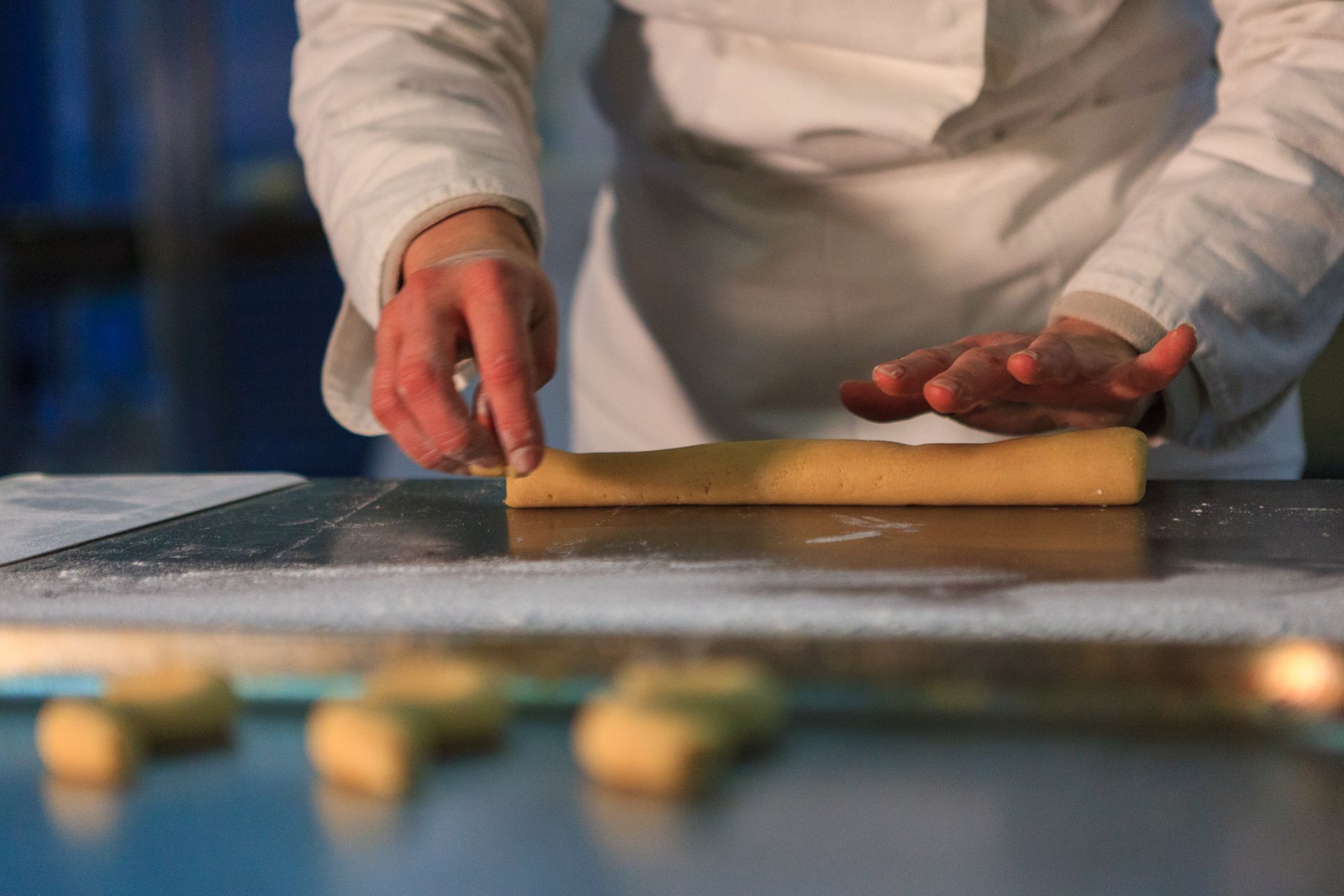 Mani che stendono la pasta con un mattarello di legno su un piano di lavoro infarinato.