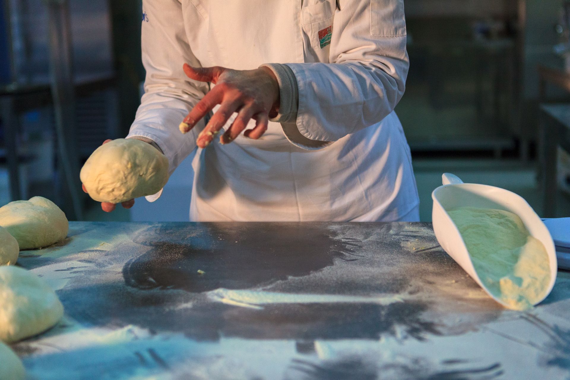 Una persona modella l'impasto su un tavolo infarinato, con due pezzi di impasto nelle vicinanze.