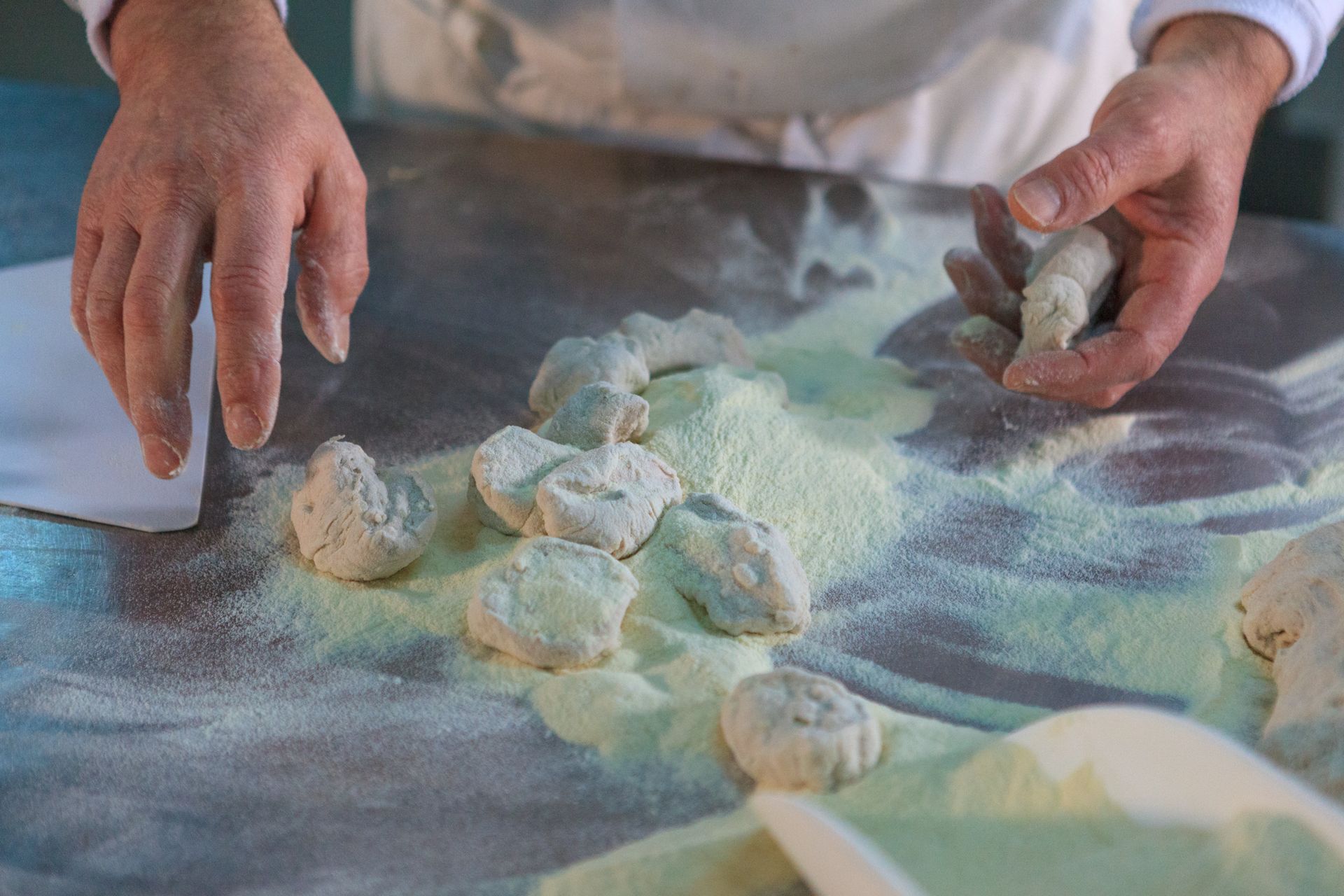 Mani che modellano pezzi di pasta infarinati su una superficie di lavoro