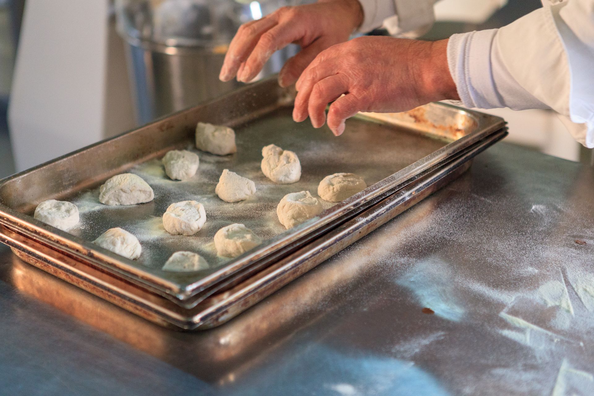 Mani che dispongono palline di impasto su una teglia infarinata in cucina
