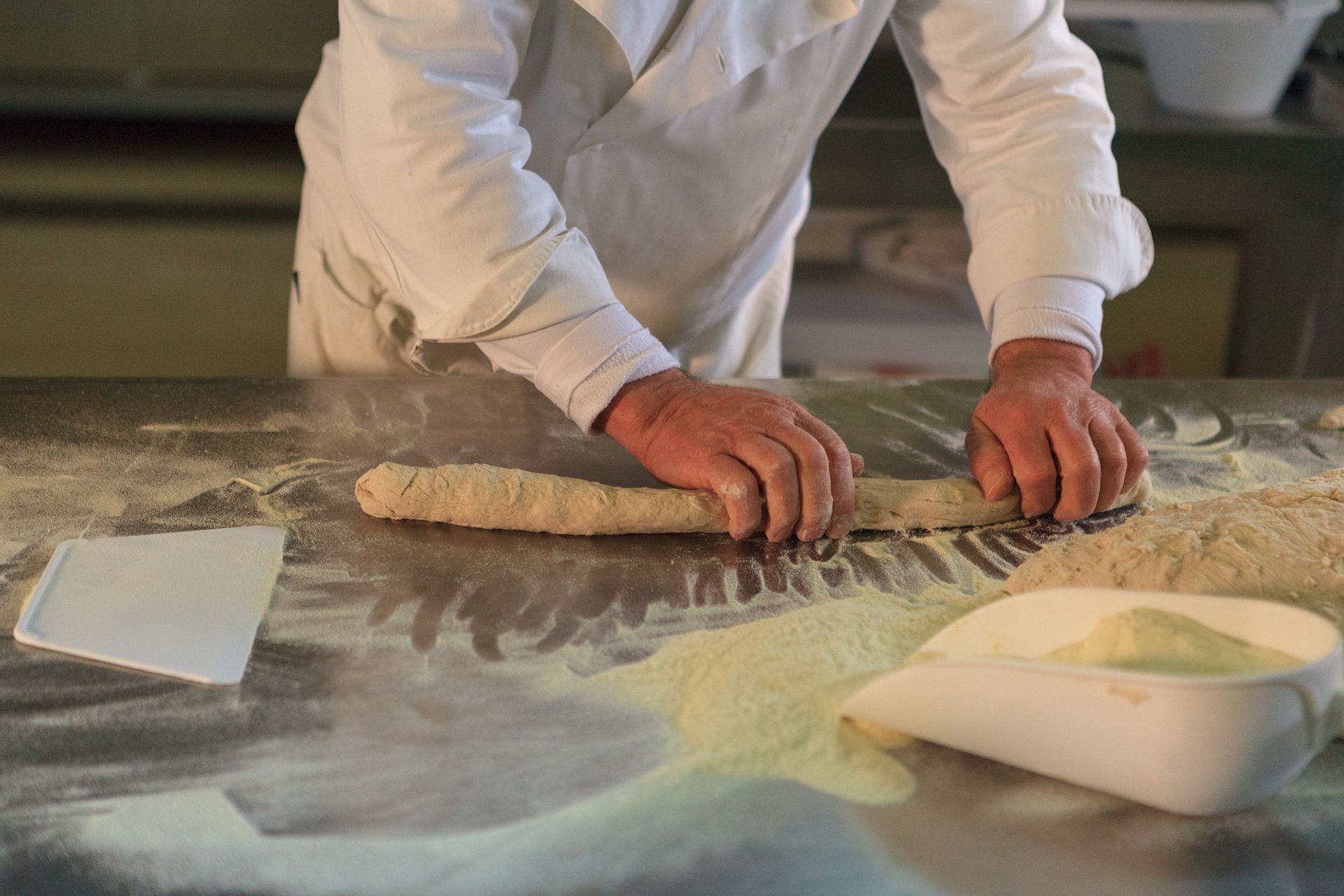 Una persona impasta la pasta su un piano di lavoro cosparso di farina, con una ciotola di farina nelle vicinanze.