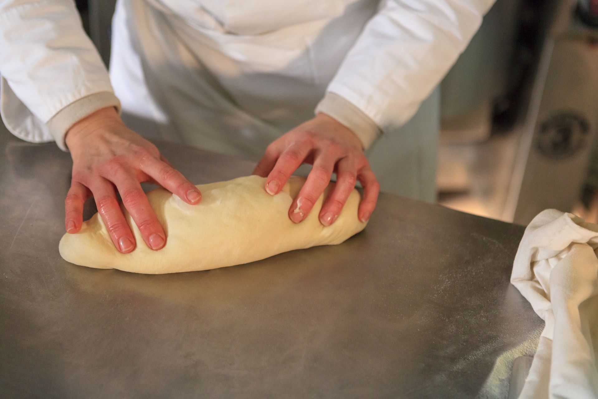 Mani che impastano la pasta su un bancone in acciaio inossidabile in una cucina