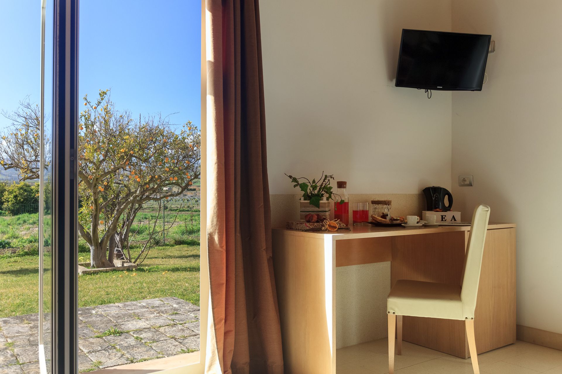 Una piccola scrivania e una sedia accanto a una finestra che si affaccia su un giardino soleggiato.