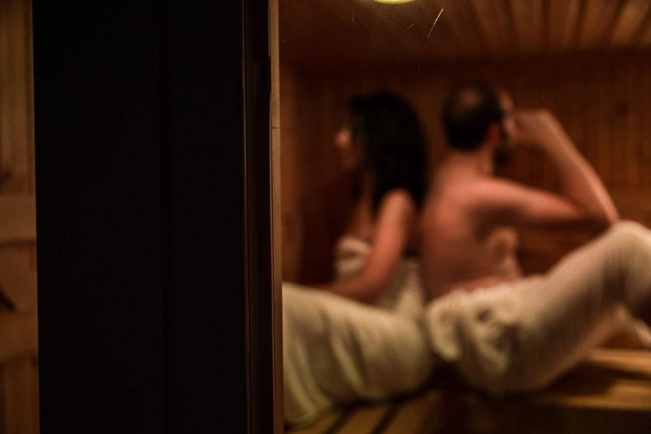 Due persone si baciano a lume di candela su un tavolo cosparso di petali e con uno sfondo illuminato di verde.