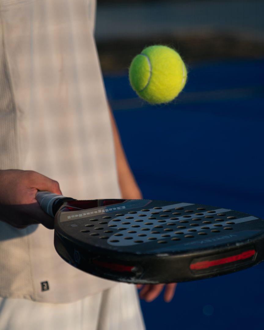 Primo piano di una persona che tiene una racchetta mentre una pallina da tennis gialla galleggia nelle vicinanze su un campo.