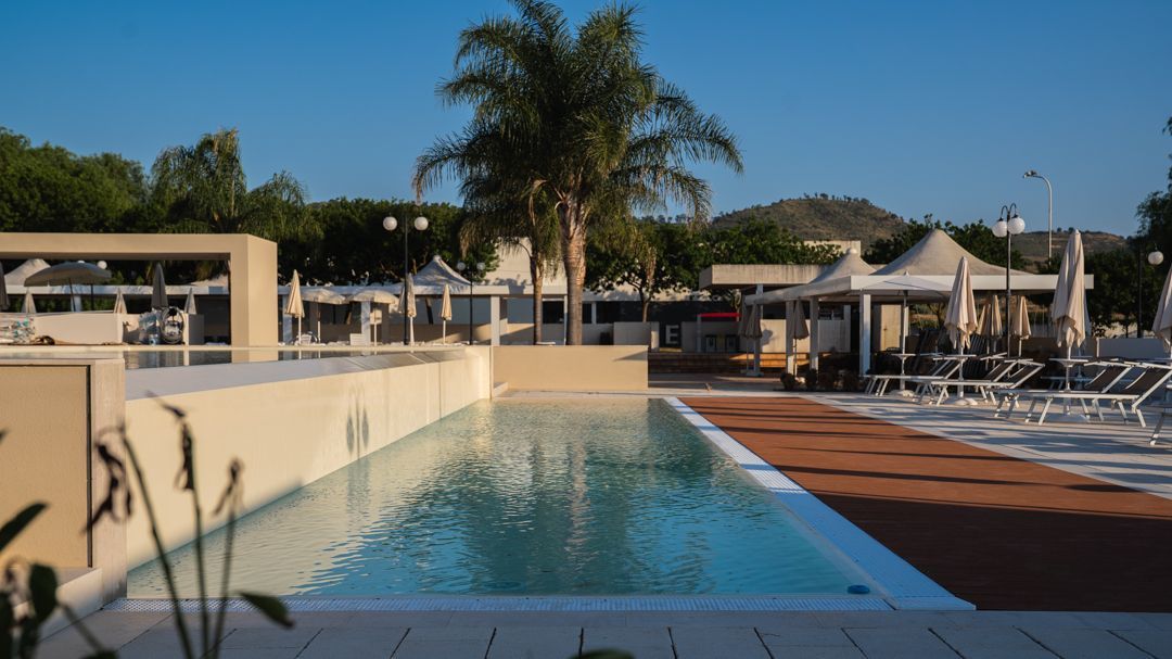 Piscina del resort con palme, lettini e acqua cristallina sotto un cielo soleggiato
