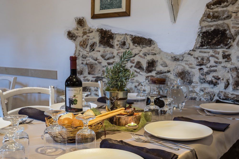 Apparecchiate la tavola con vino, pane e piatti accanto a un rustico muro di pietra.