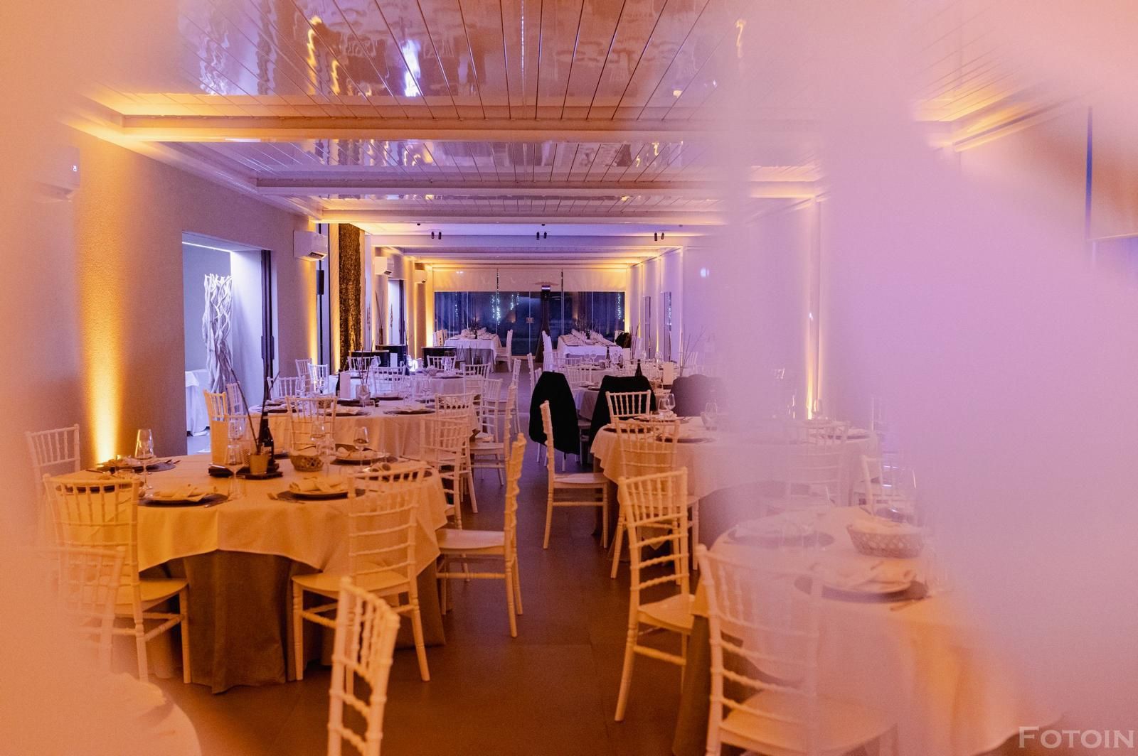 Elegante sala per banchetti con sedie bianche, tavoli rotondi e luci calde rosa-violacee.