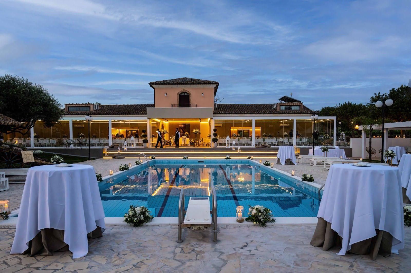 Elegante terrazza a bordo piscina al tramonto, con padiglione illuminato e tavolini da cocktail.