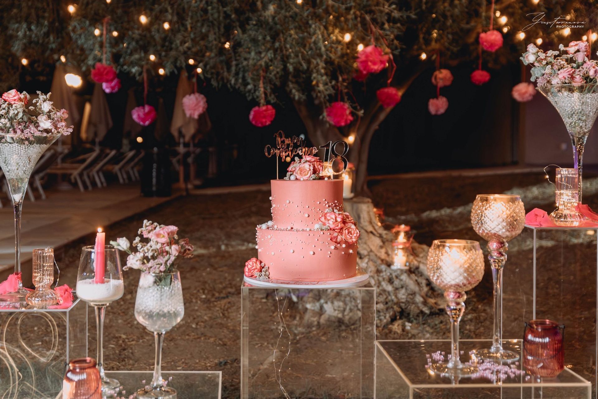 Torta a più piani rosa su un tavolo a specchio con decorazioni floreali e candele in una romantica ambientazione all'aperto.