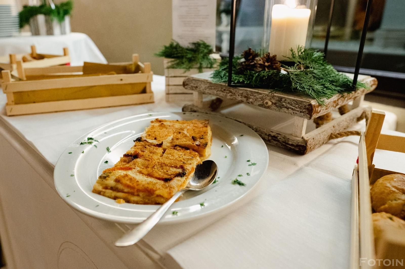 Pesce grigliato impiattato su un tavolo con candela accesa, piante e cestini di pane.