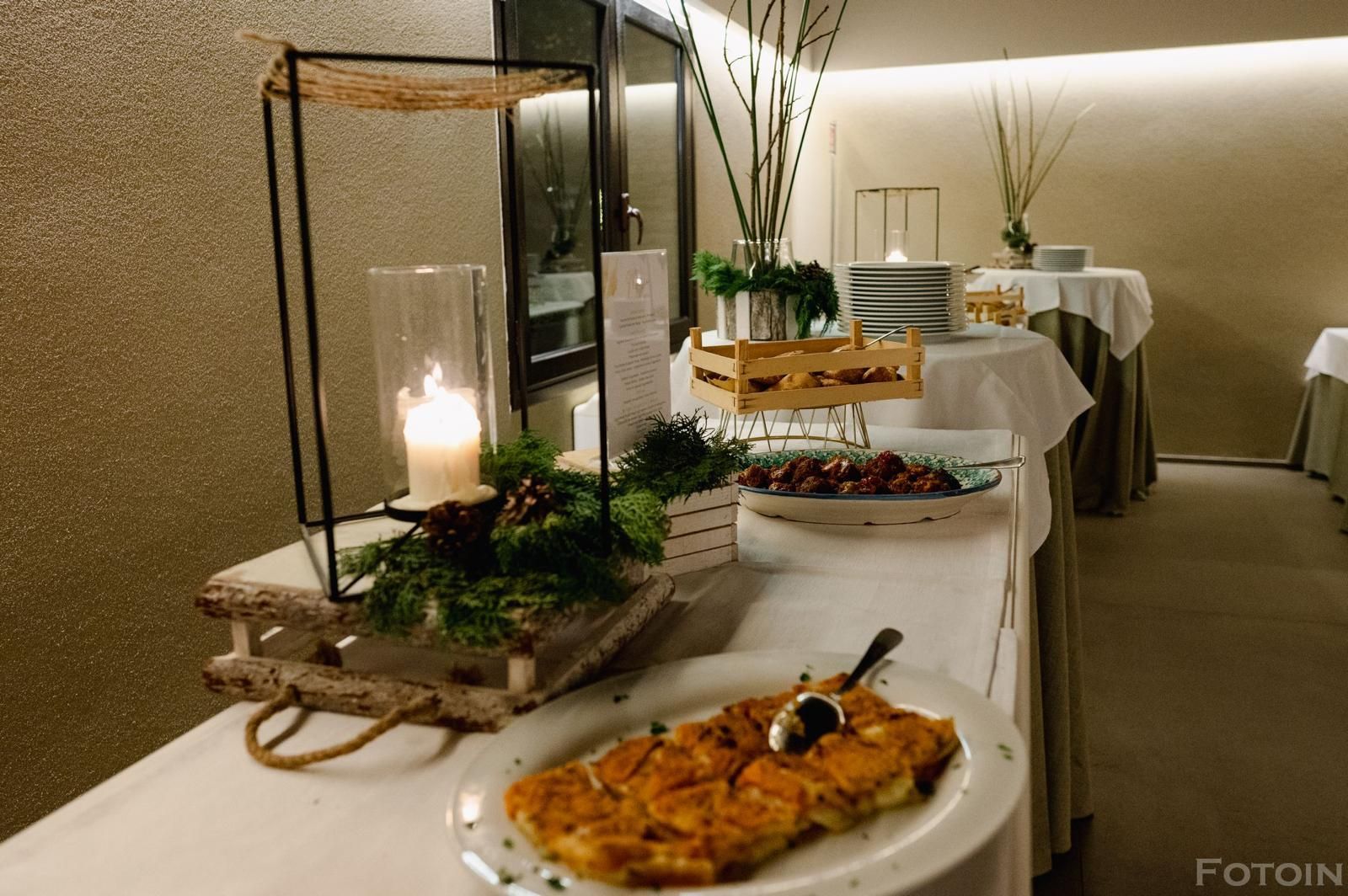 Tavolo da buffet con candele, piante, pasticcini e un piatto impiattato in una sala da banchetto illuminata da luci soffuse.