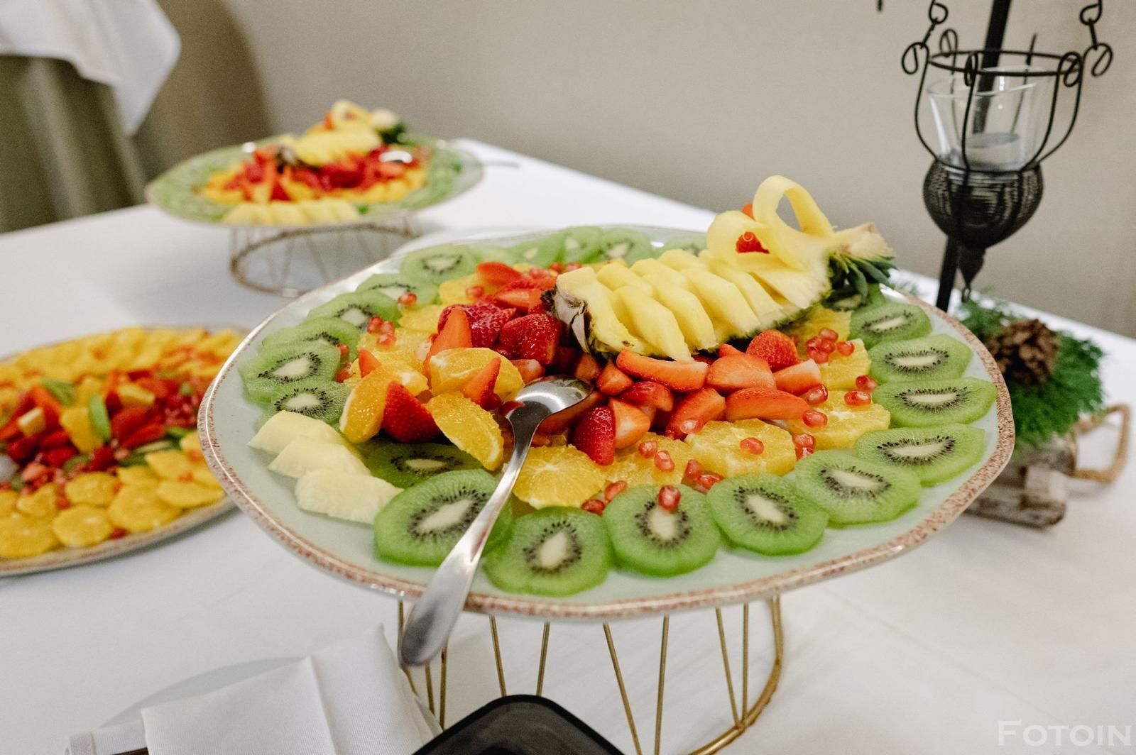 Piatto di frutta colorato con kiwi, ananas, fragole e mele su un supporto decorativo da tavolo.