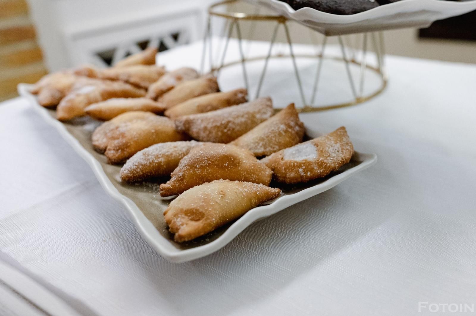 Pasticcini in zucchero a velo su un piatto da portata bianco con un supporto decorativo in filo metallico sullo sfondo.