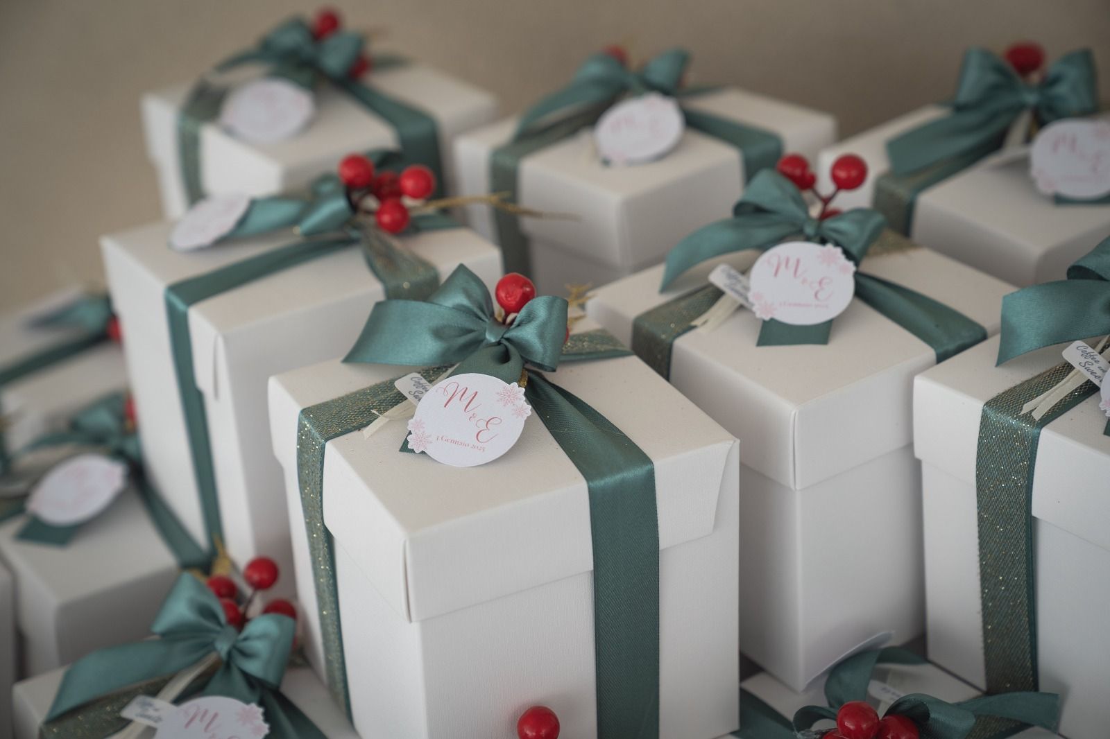 Scatole regalo bianche impilate, legate con un nastro verde e decorate con bacche rosse.
