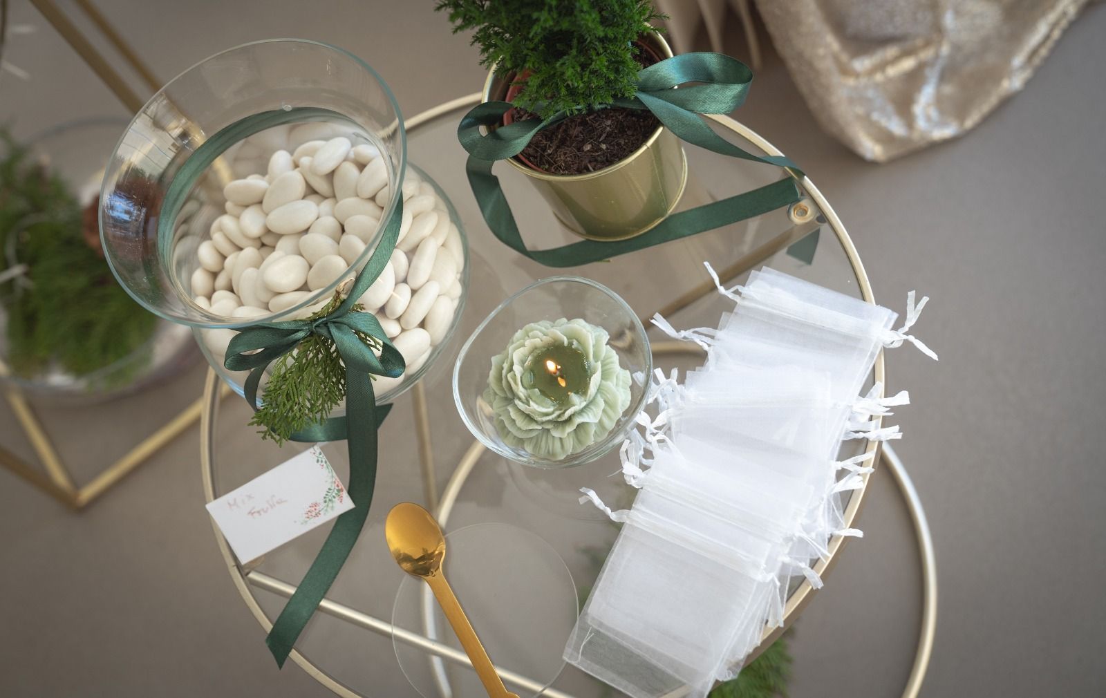 Una ciotola di vetro con caramelle bianche, un nastro verde e delle candeline su un vassoio dorato.