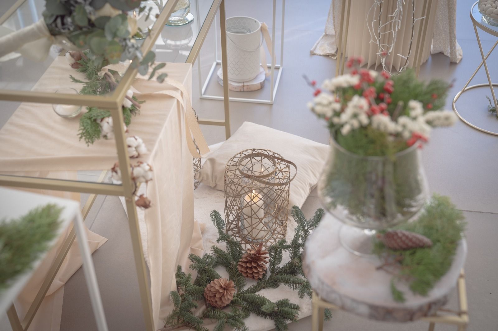 Composizione floreale dai colori pastello con mensole bianche, piante e una lanterna di vimini su un tavolo.